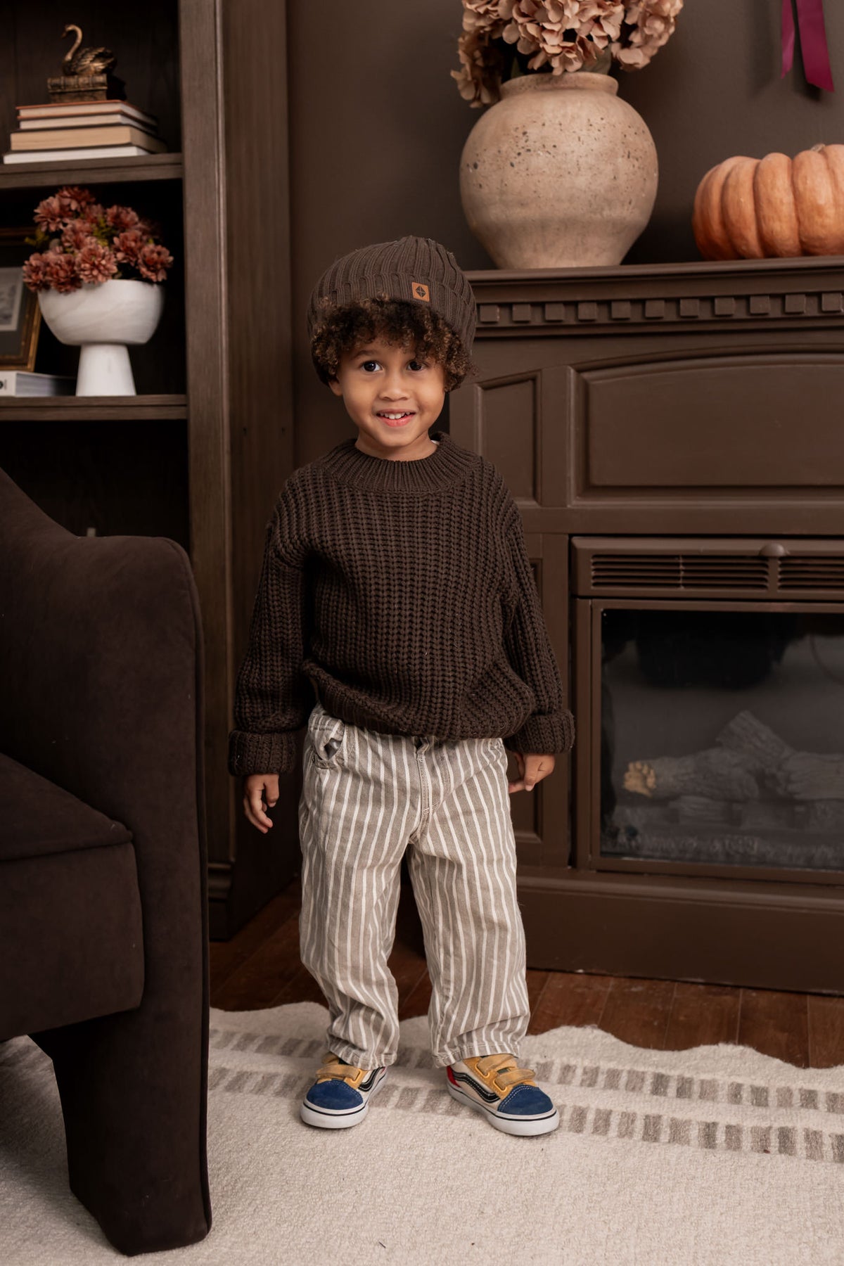 Boy standing in a living room wearing Chunky Knit Sweater and chunky knit ribbed beanie in espresso over pants