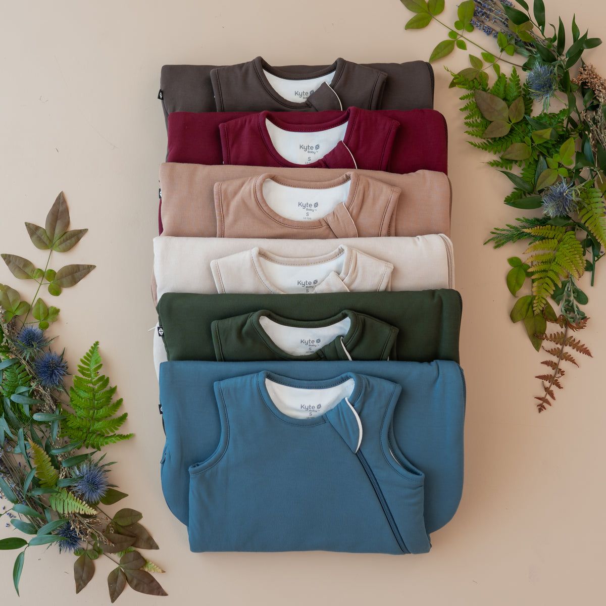 Stack of kyte baby folded sleep bags with a natural leafy background
