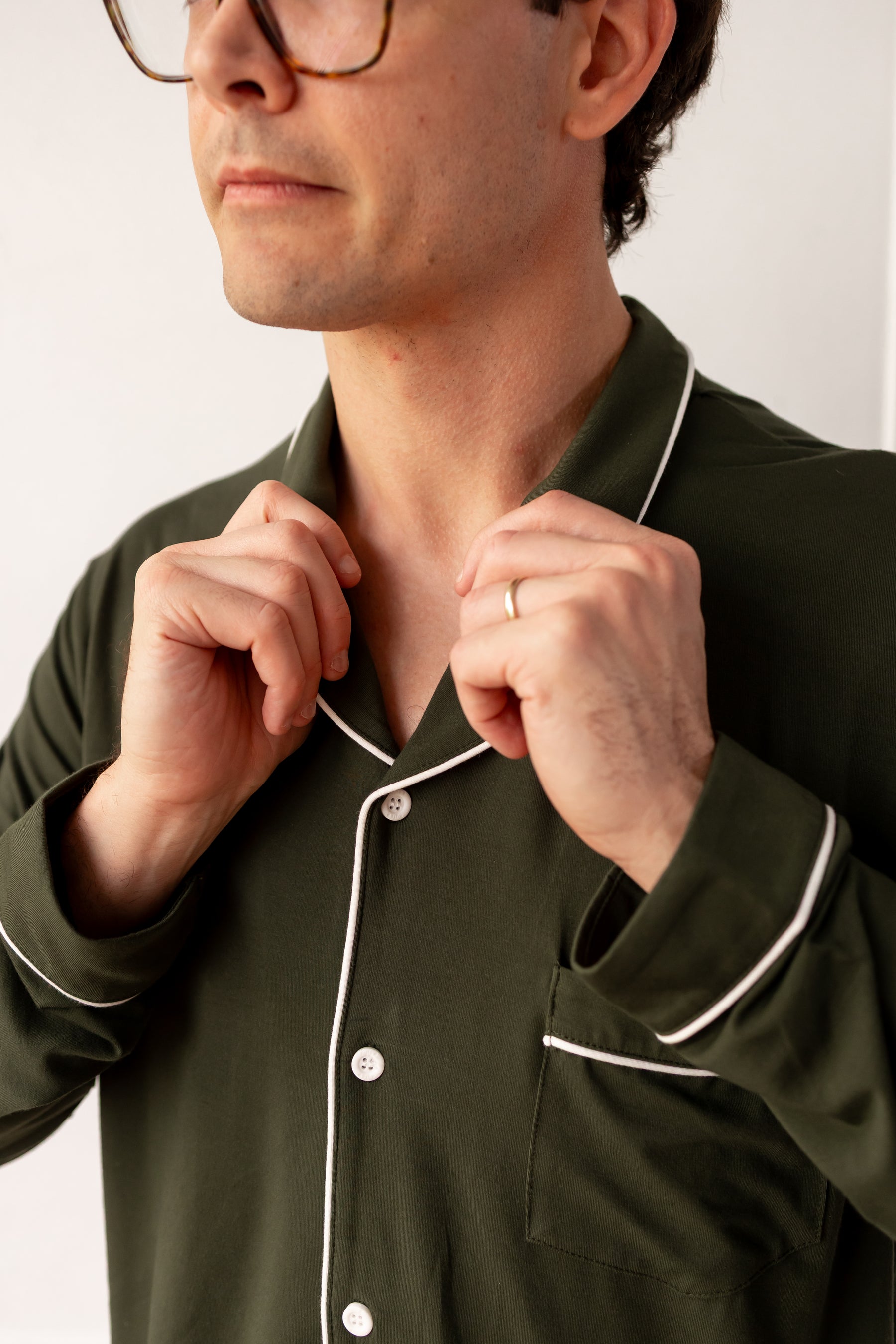 Man wearing a green pajama set with white piping, adjusting the collar.
