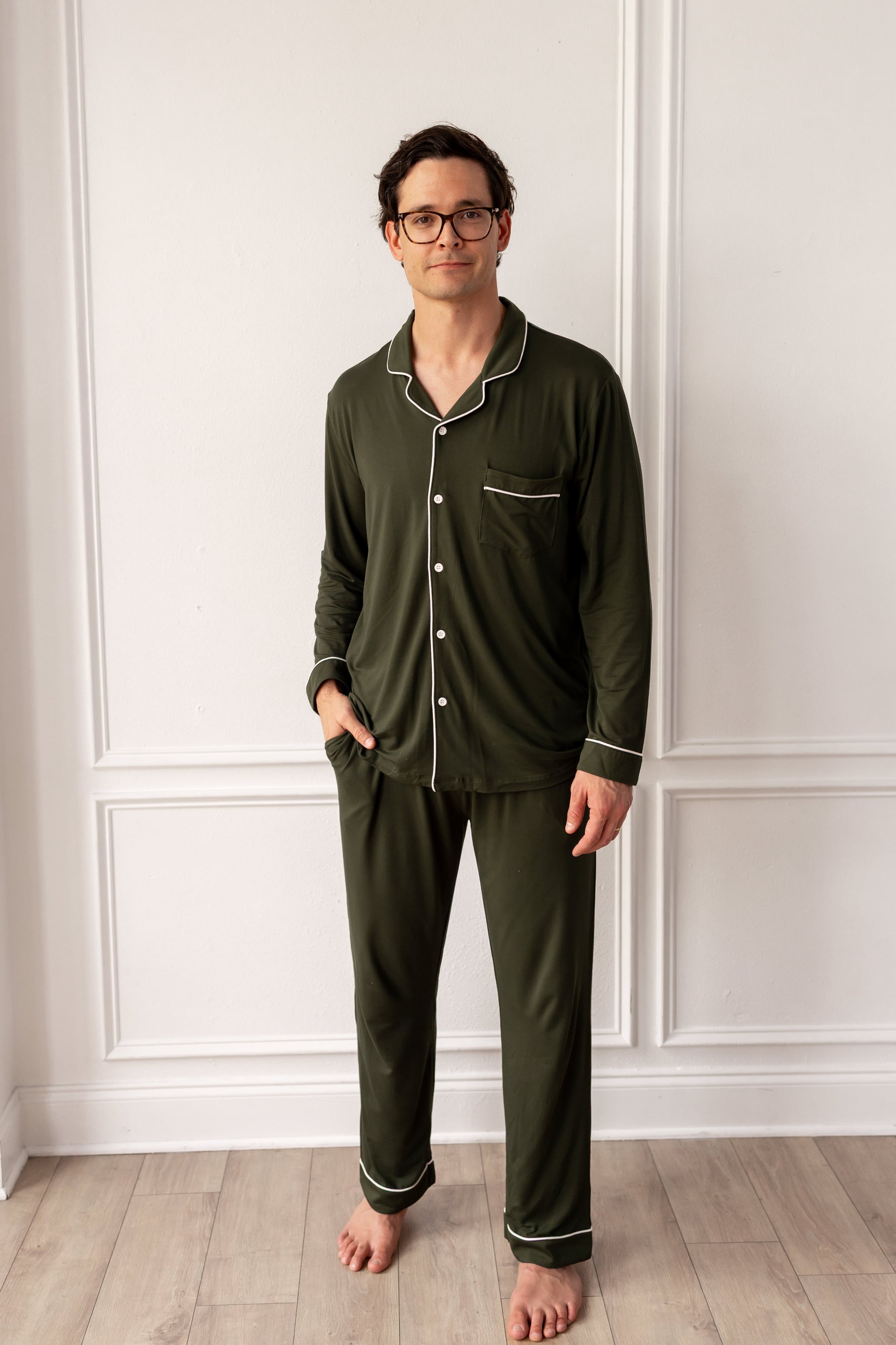 Man wearing green pajamas standing against a white paneled wall.