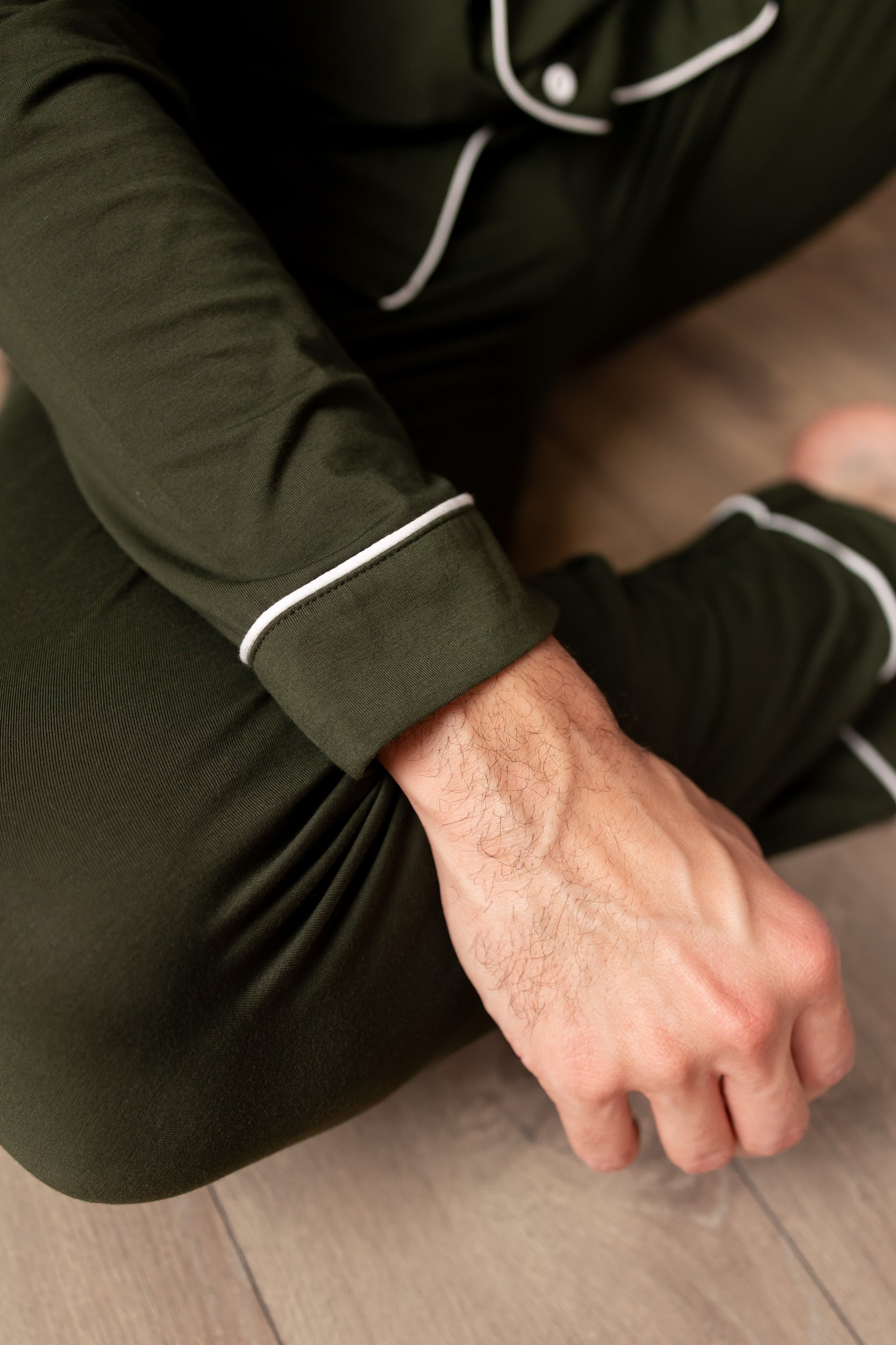 Person wearing dark green pajama set with white trim sitting on a wooden floor.