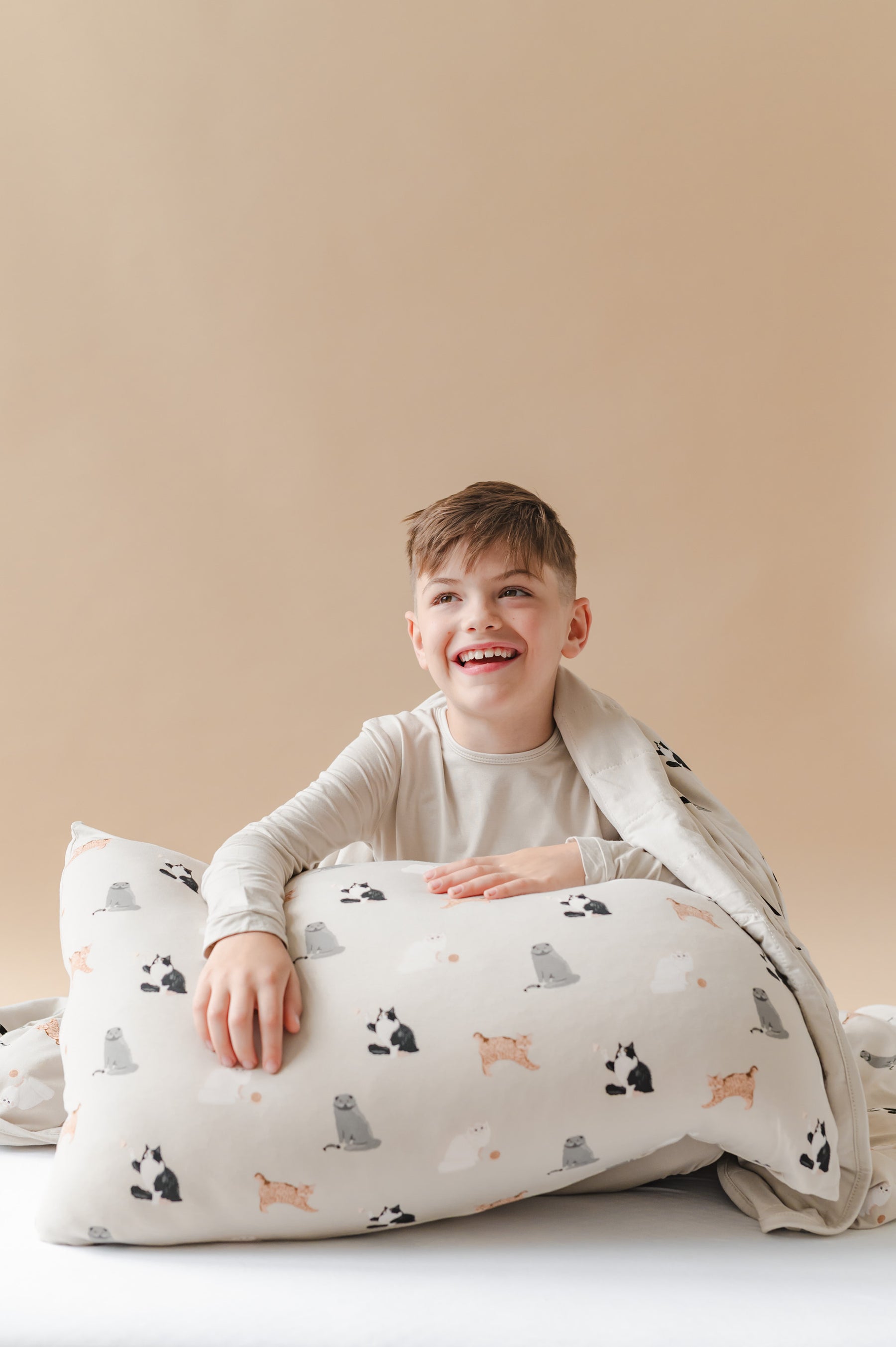 Child sitting on a bed with a cat patterned pillow and blanket against a beige wall.
