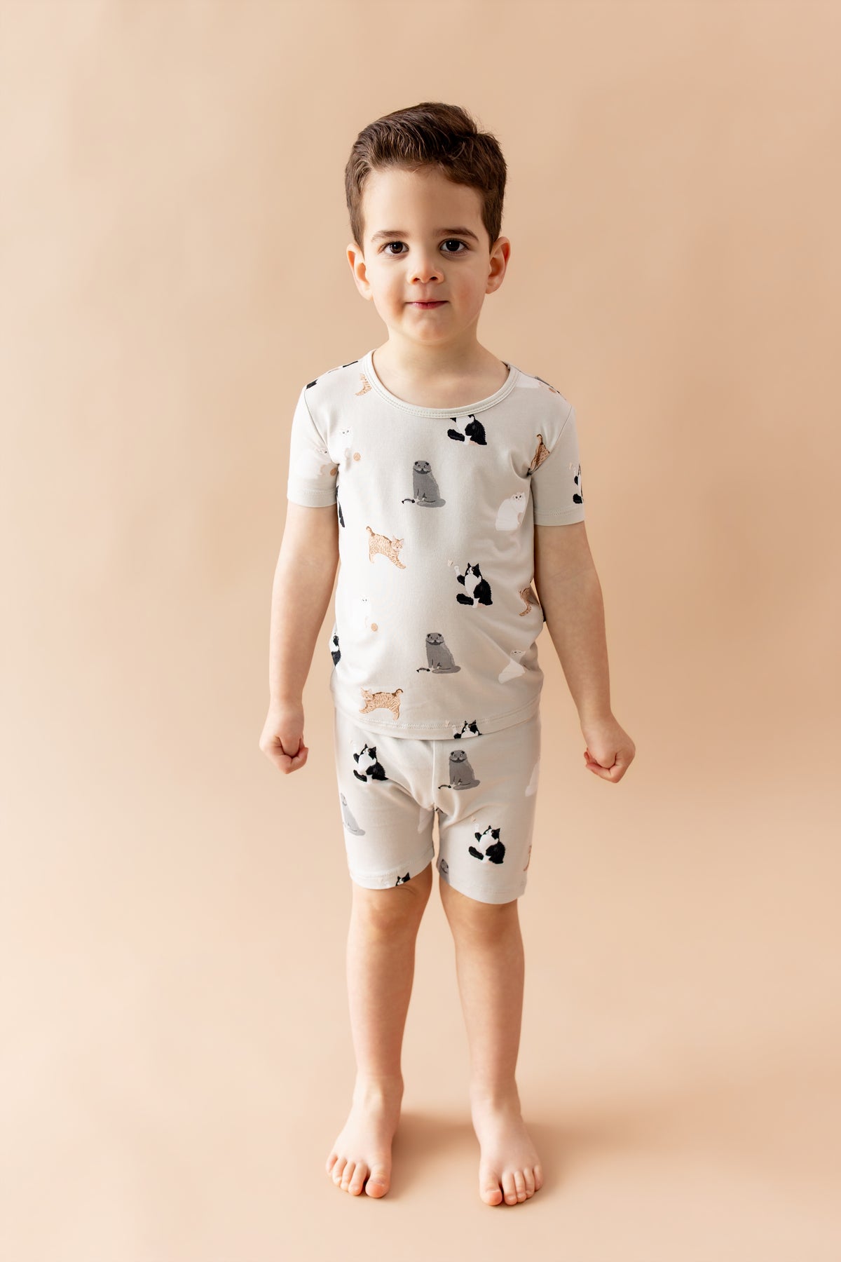 Young boy standing in front of a light beige background wearing the Short Sleeve Pajamas in Fluffy Cat