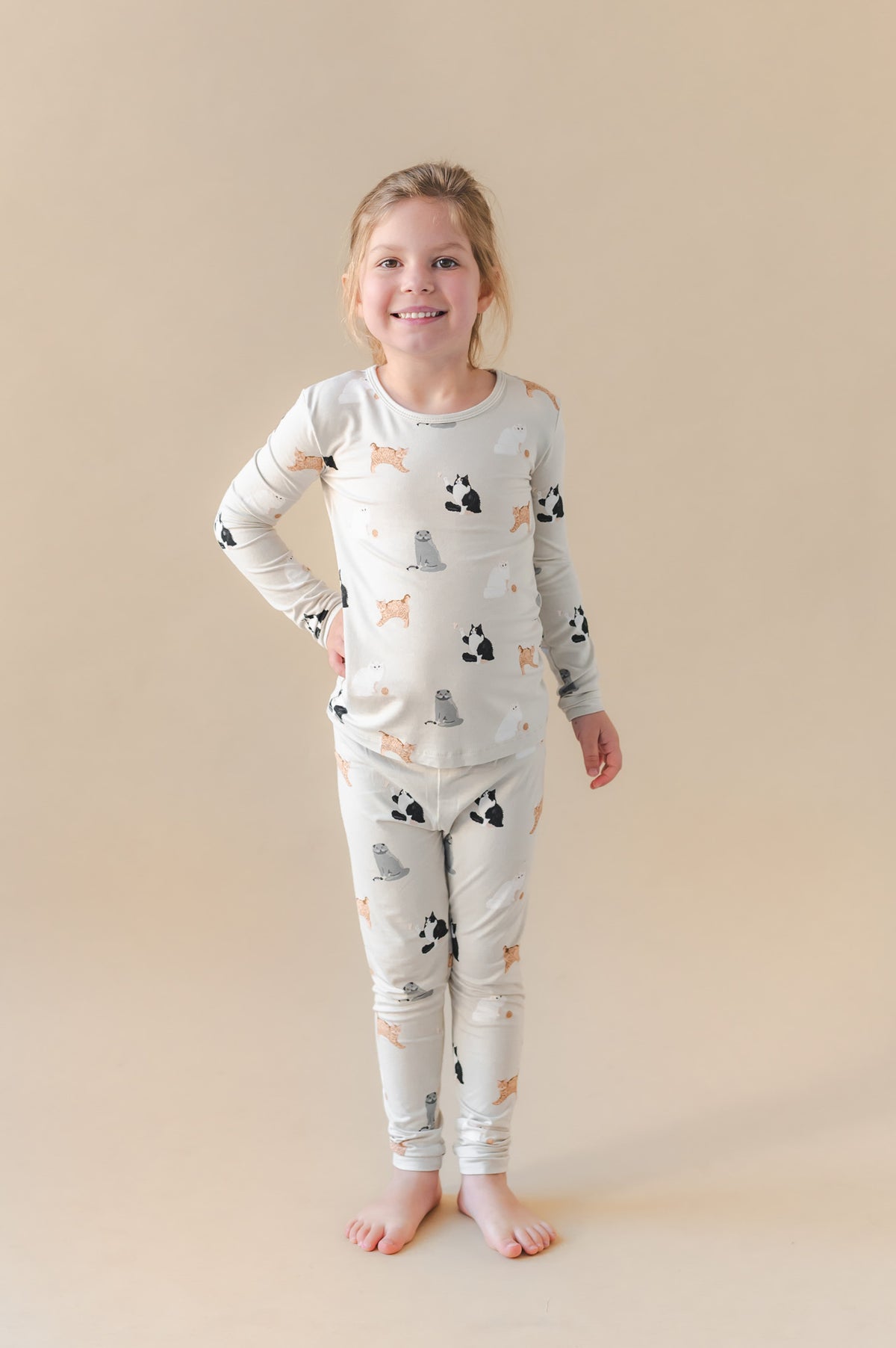Young girl wearing a pajama set with cat prints on a beige background