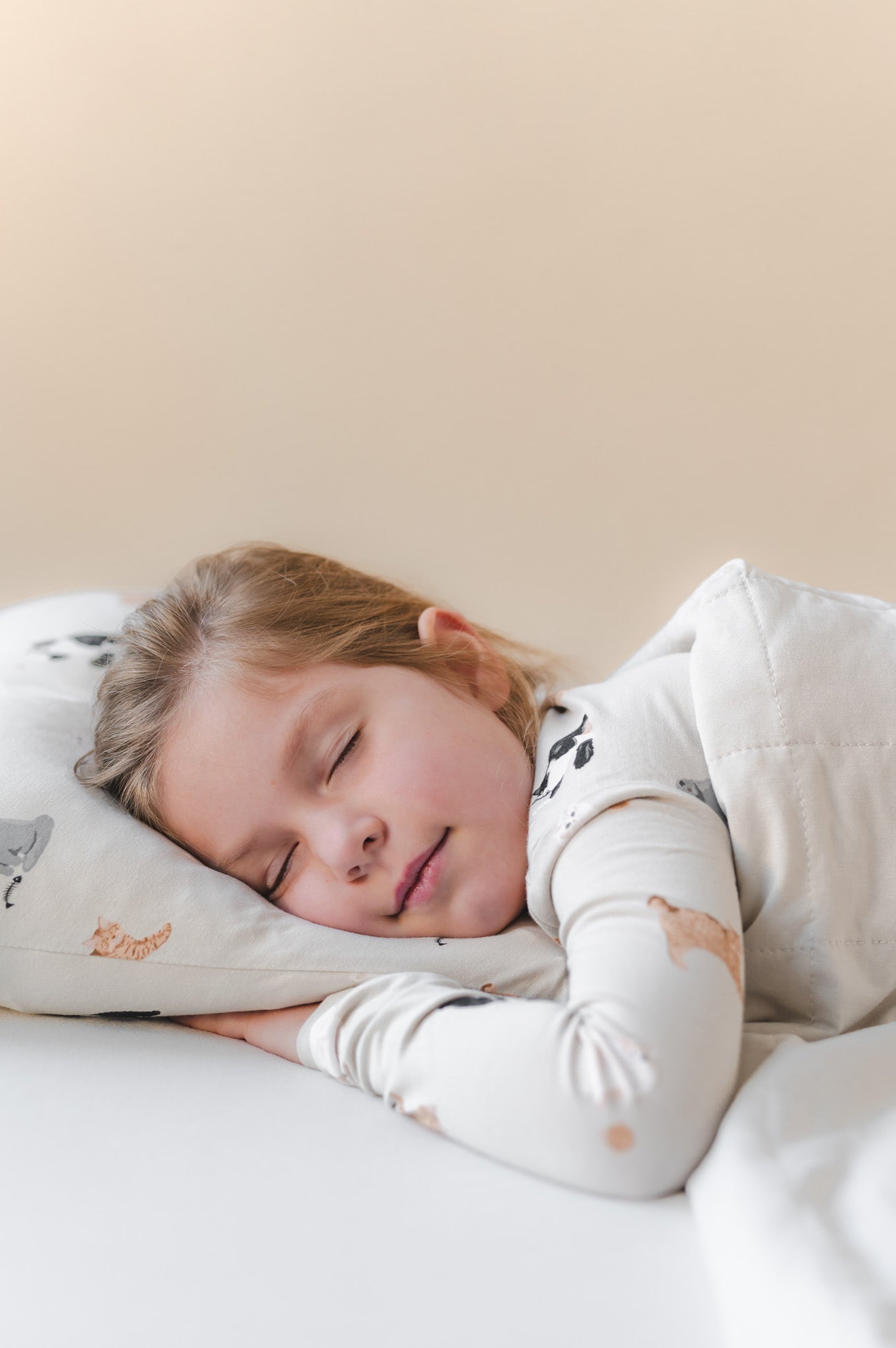 Child sleeping on a cat printed pillow with a neutral background