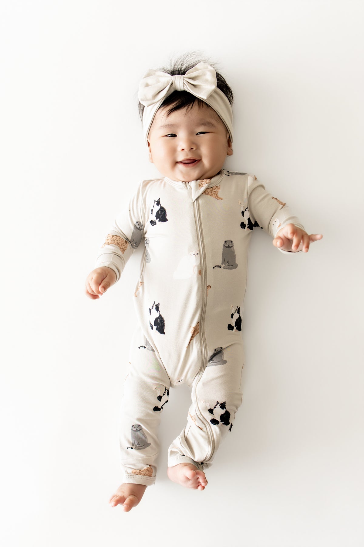Infant girl wearing the Zippered Romper in Fluffy Cat with light beige bow