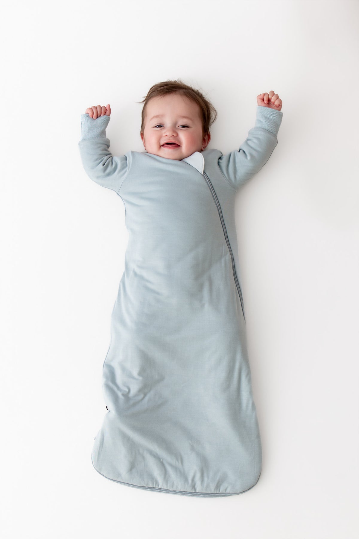 Baby wearing a long sleeve wearable blanket in a light blue color laying on a white surface