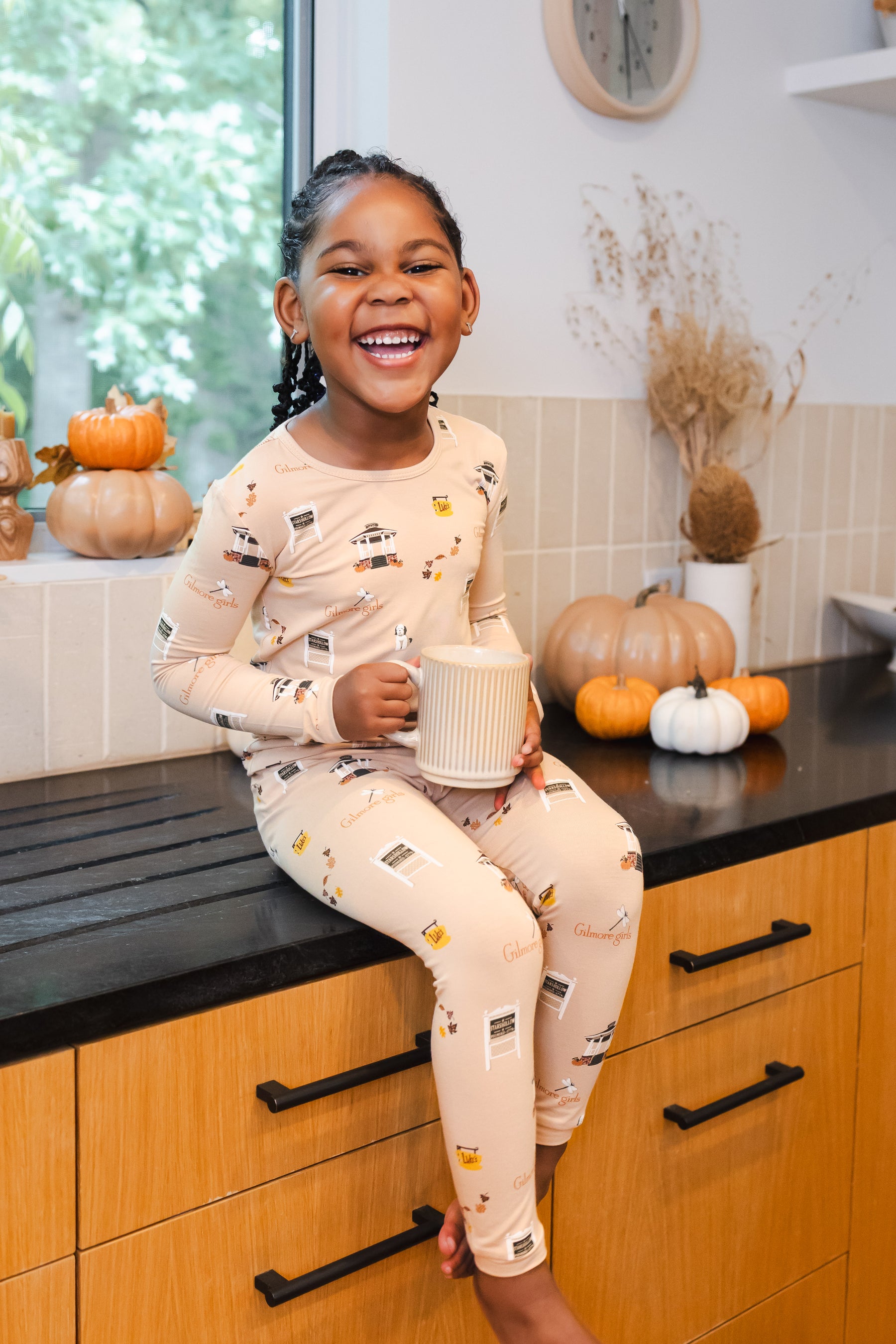 Child in Gilmore Girls pajamas sitting on a kitchen counter with pumpkins in the background