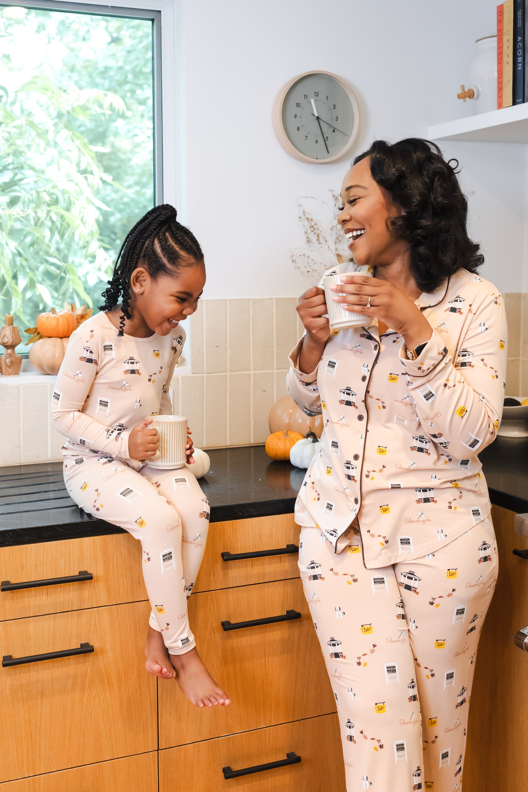 Woman and child in matching Gilmore Girls pajamas sitting on a kitchen counter, enjoying coffee.