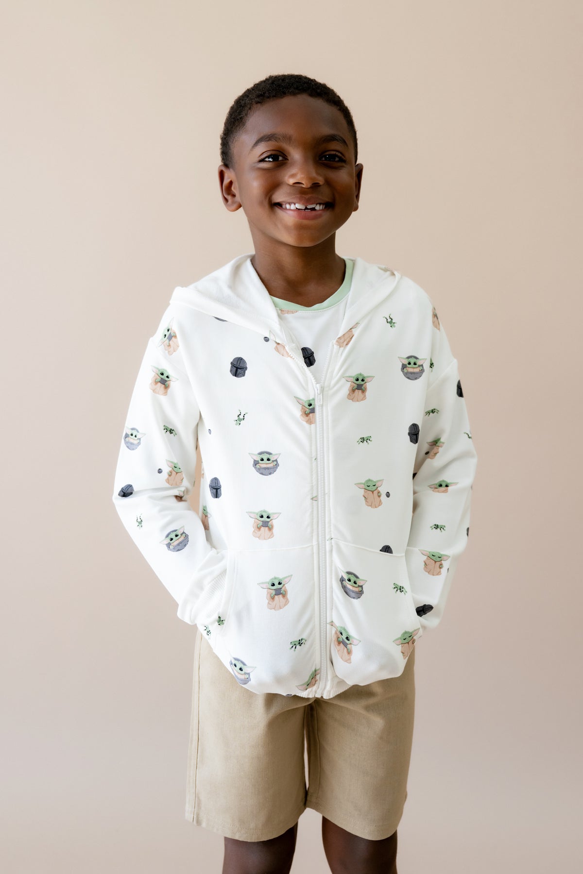 Young boy wearing the Zip-Up Hoodie in Grogu™ with his hands in the pockets and the hood down