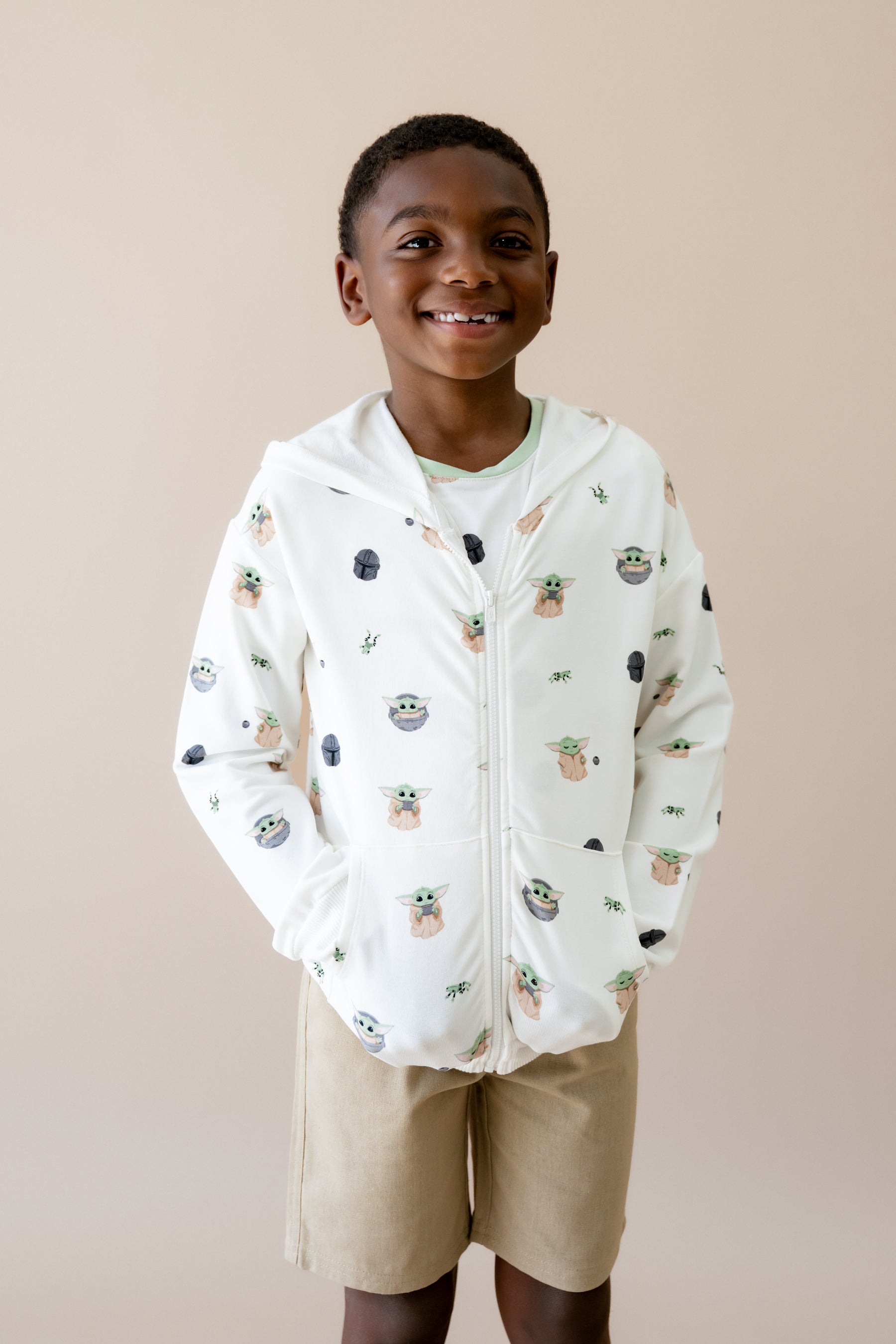 Young boy wearing the Zip-Up Hoodie in Grogu™ with his hands in the pockets and the hood down