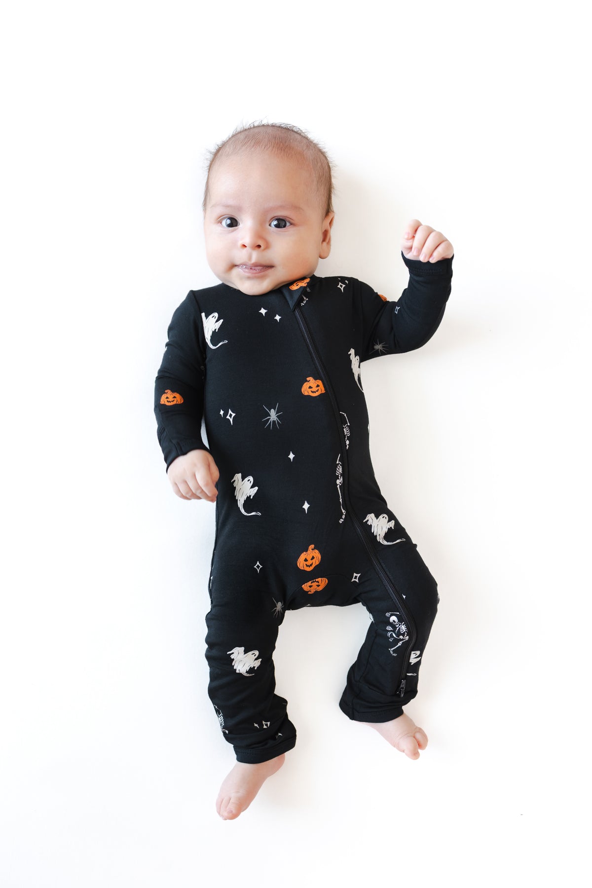 Baby wearing Zippered Romper in Halloween Friends print lying on a white background