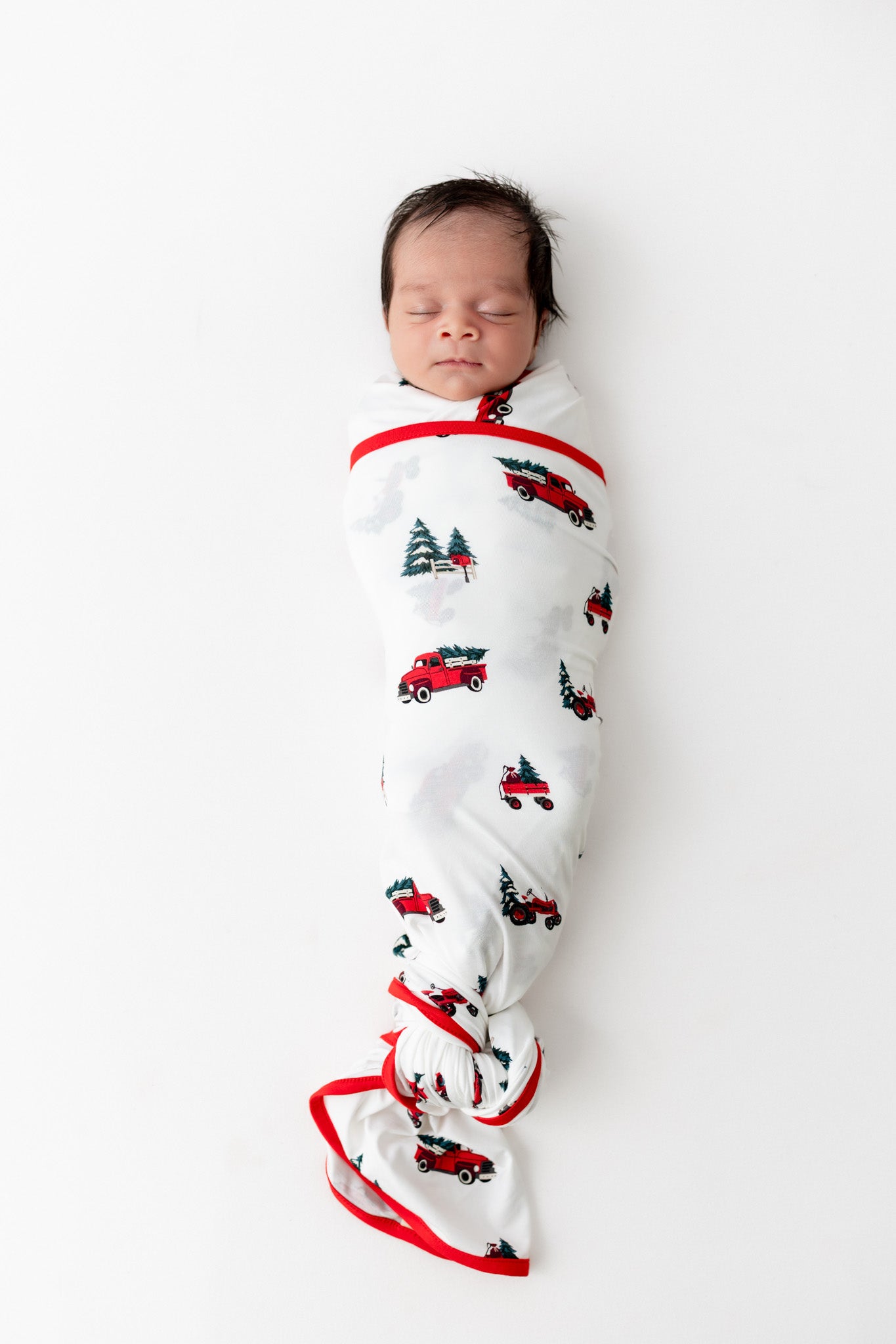 Baby wearing Swaddle Blanket in holiday farm tree print on a beige background