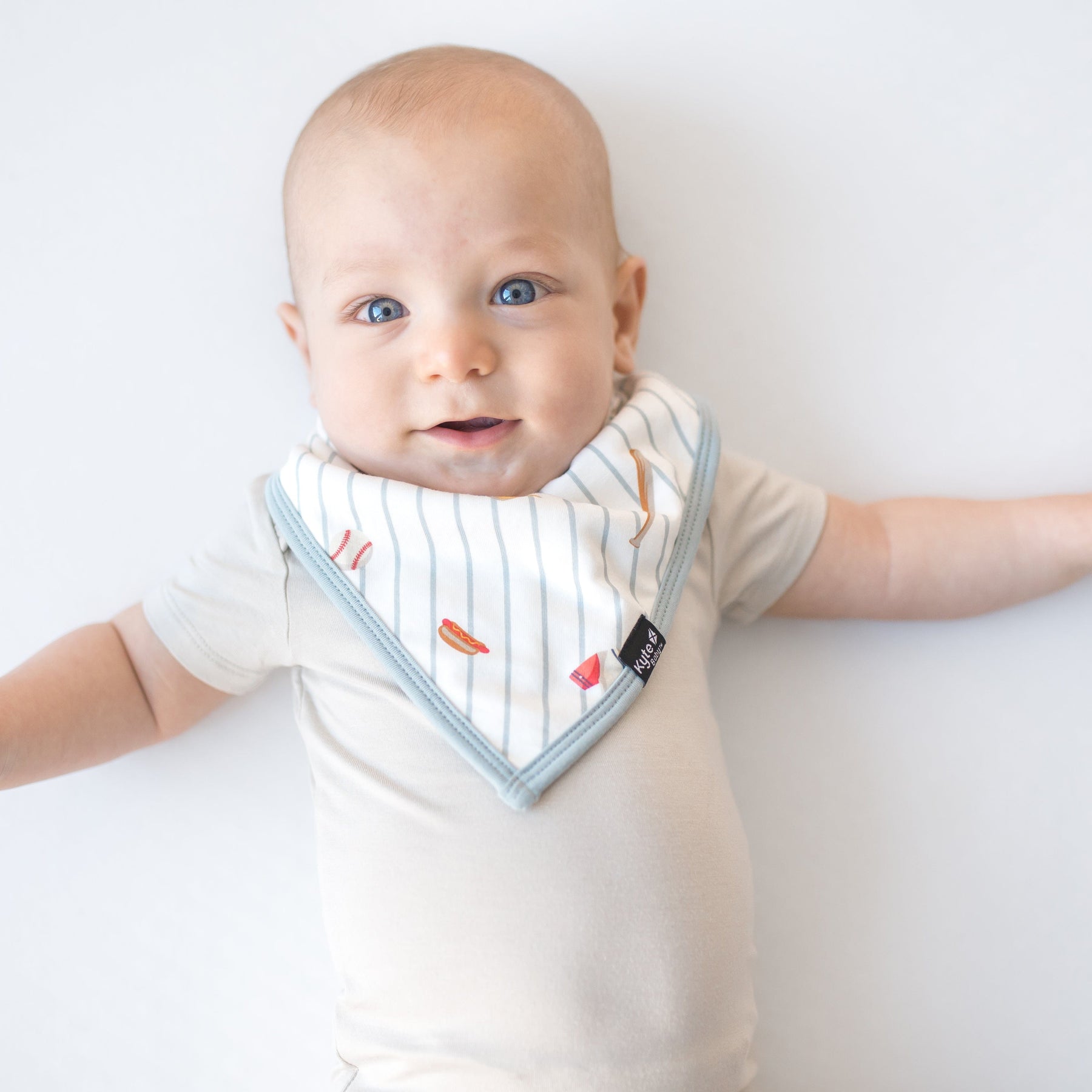 Young baby wearing the Bib in Home Run overtop a light cream short sleeve bodysuit