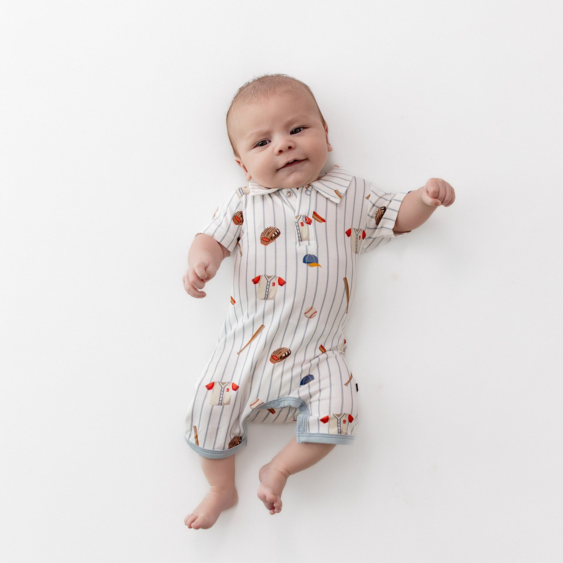 Young infant laying on a light neutral background wearing the Polo Shortall in Home Run