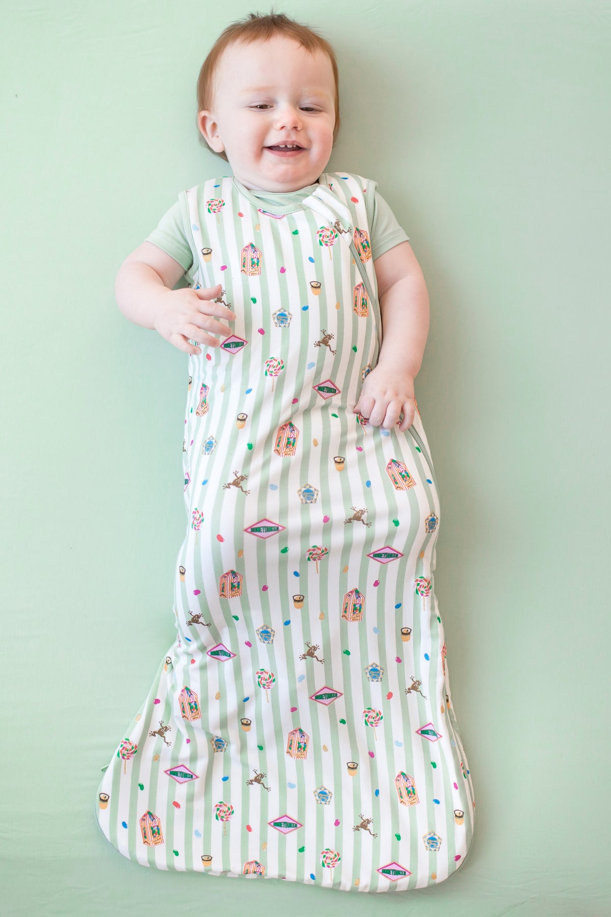 Baby wearing a green and white striped sleep bag with colorful Harry Potter patterns on a green background