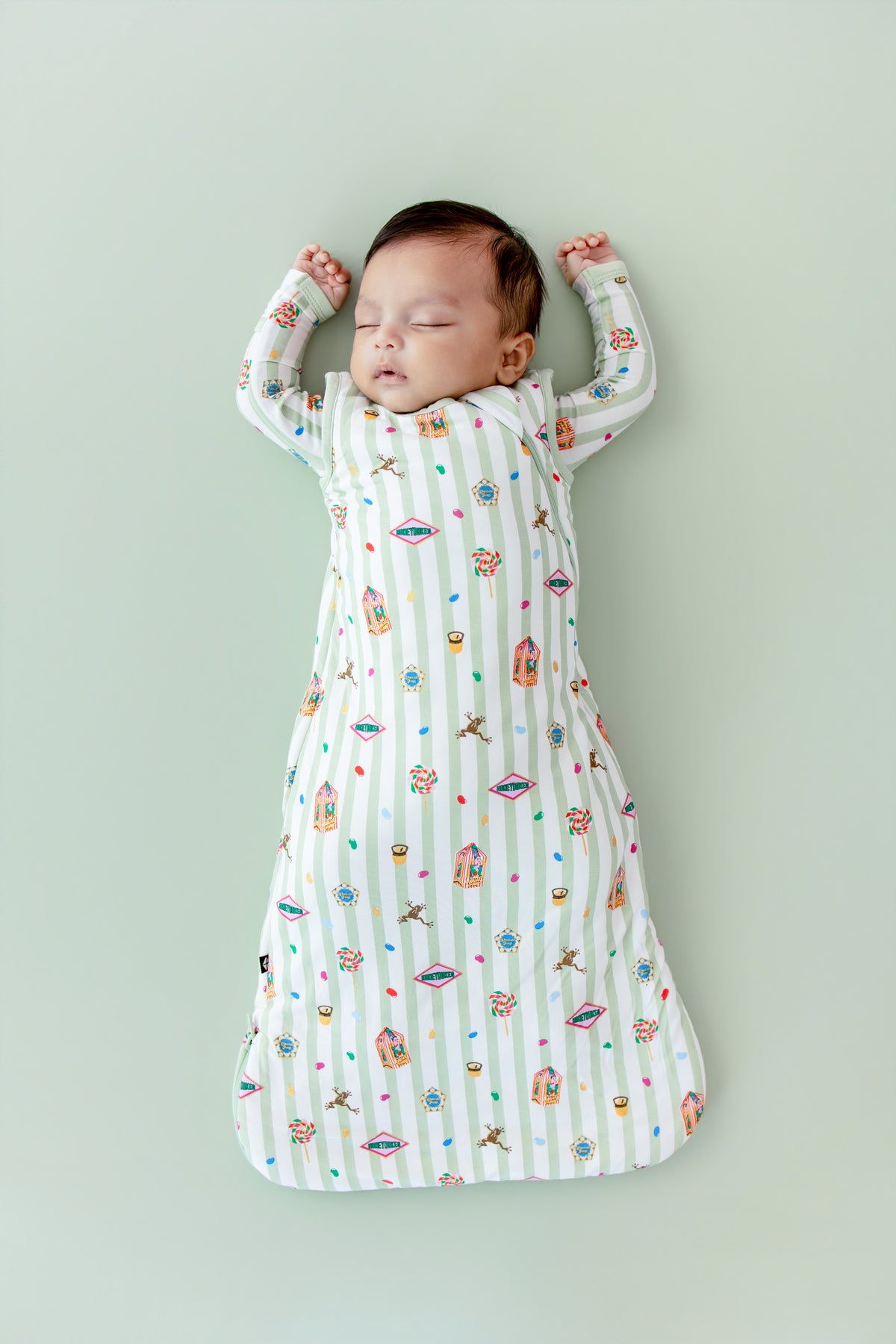 Baby asleep in a green and white striped sleep bag with colorful Harry Potter patterns on a green background