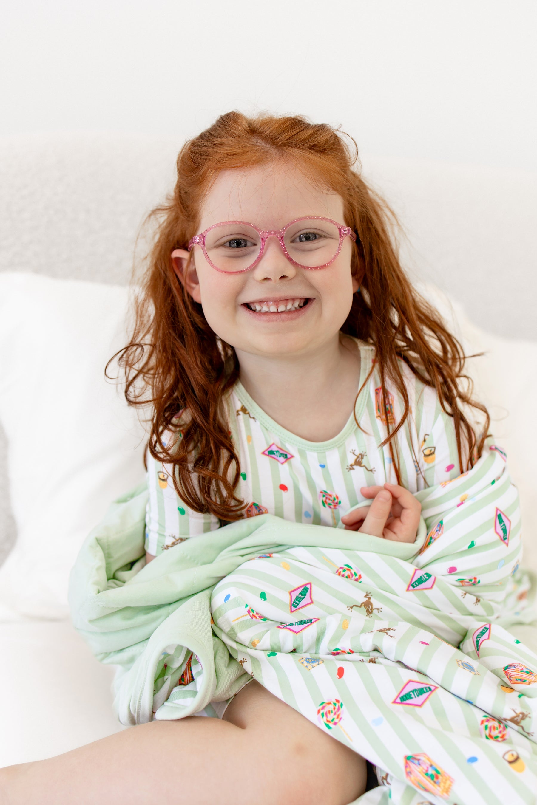 Child wrapped in a green and white striped youth blanket with colorful Harry Potter patterns wearing a similar print short sleeve pajama set