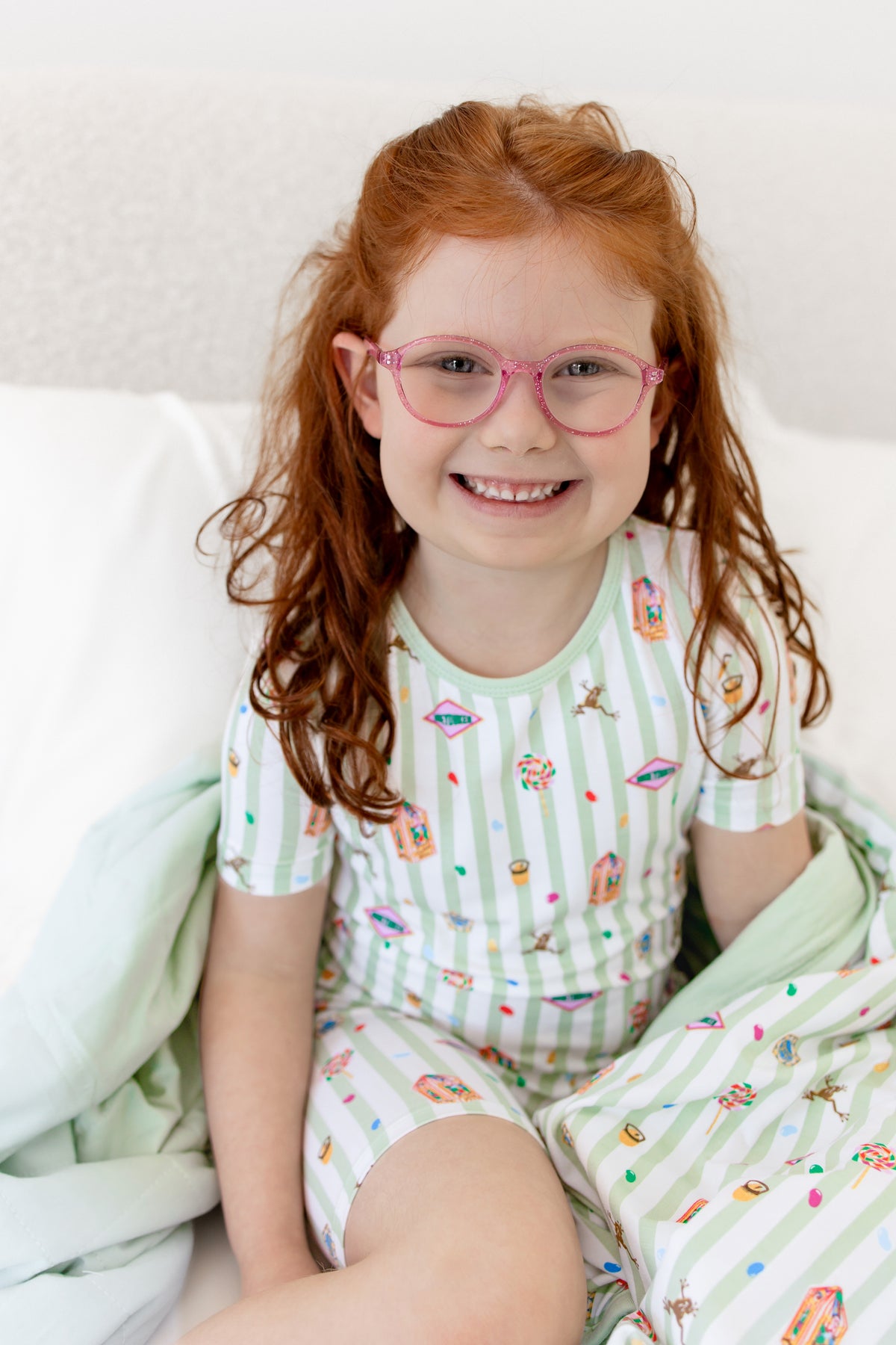 Child posing on a bed in a green and white striped youth blanket with colorful Harry Potter patterns wearing a similar print short sleeve pajama set