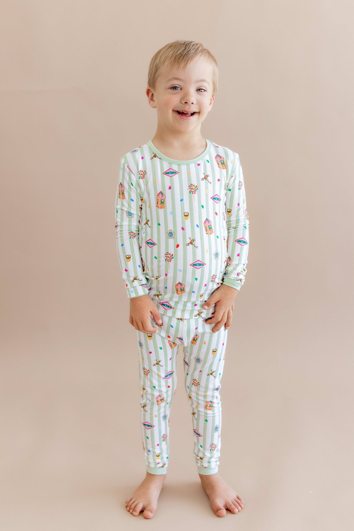 Child wearing a green and white striped long sleeve pajama set with colorful Harry Potter patterns on a beige background