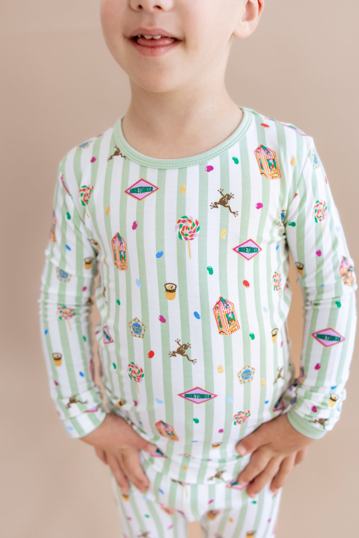 Child wearing a green and white striped long sleeve pajama set with colorful Harry Potter patterns on a beige background