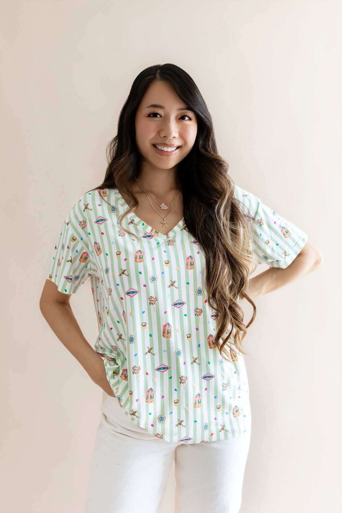 Model wearing Women's Relaxed Fit V-Neck having colorful Harry Potter patterns on a green and white striped fabric over beige pants on a beige background