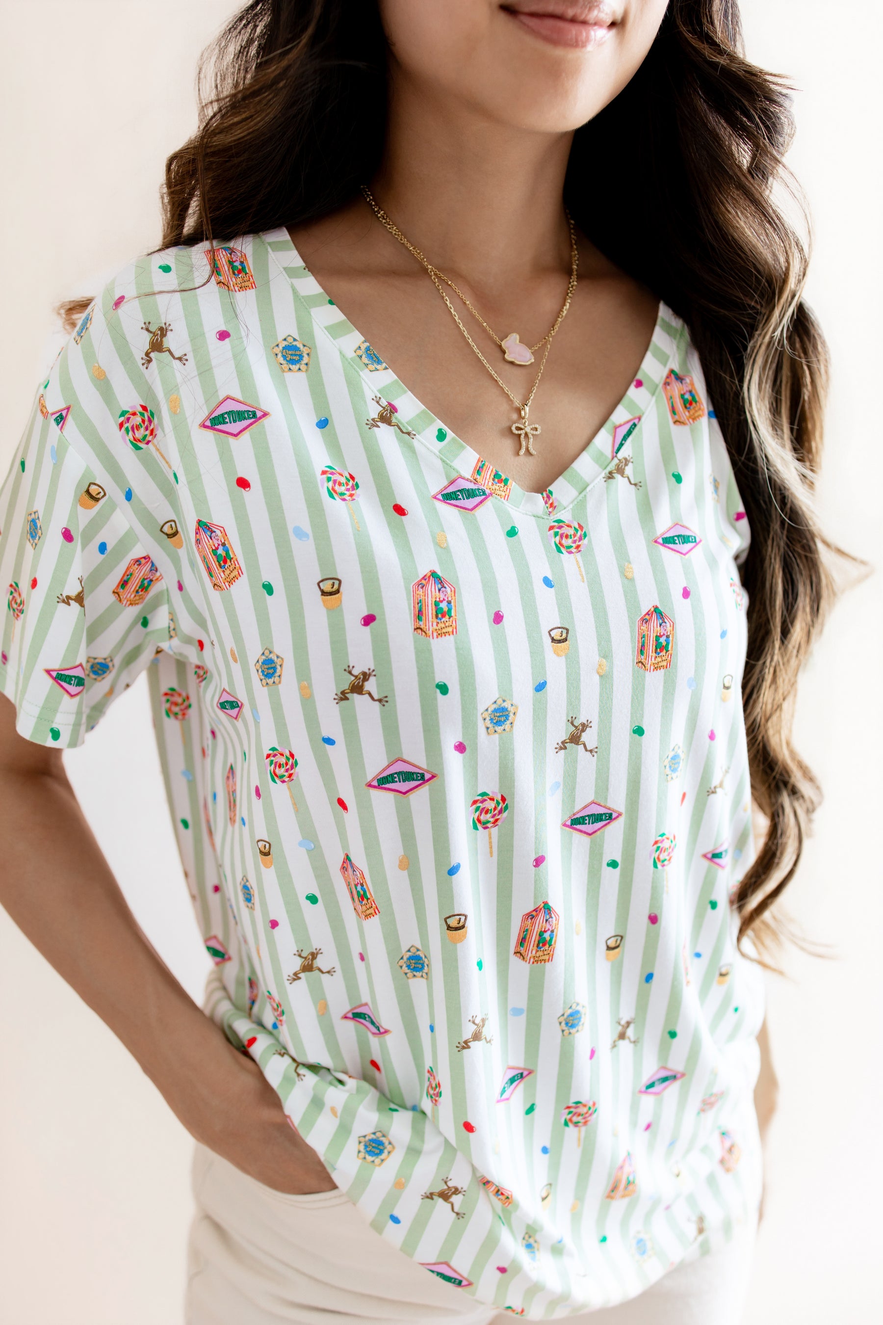 Model wearing Women's Relaxed Fit V-Neck having colorful Harry Potter patterns on a green and white striped fabric on a beige background