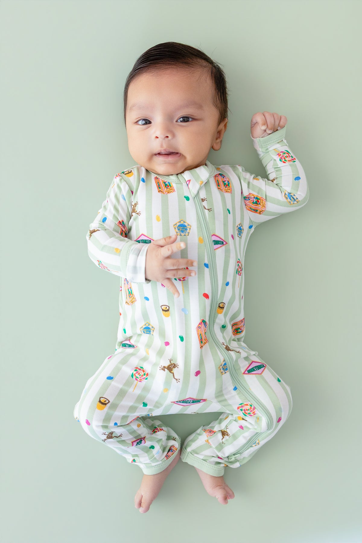 Baby wearing a green and white striped zippered romper with colorful Harry Potter patterns on a green background