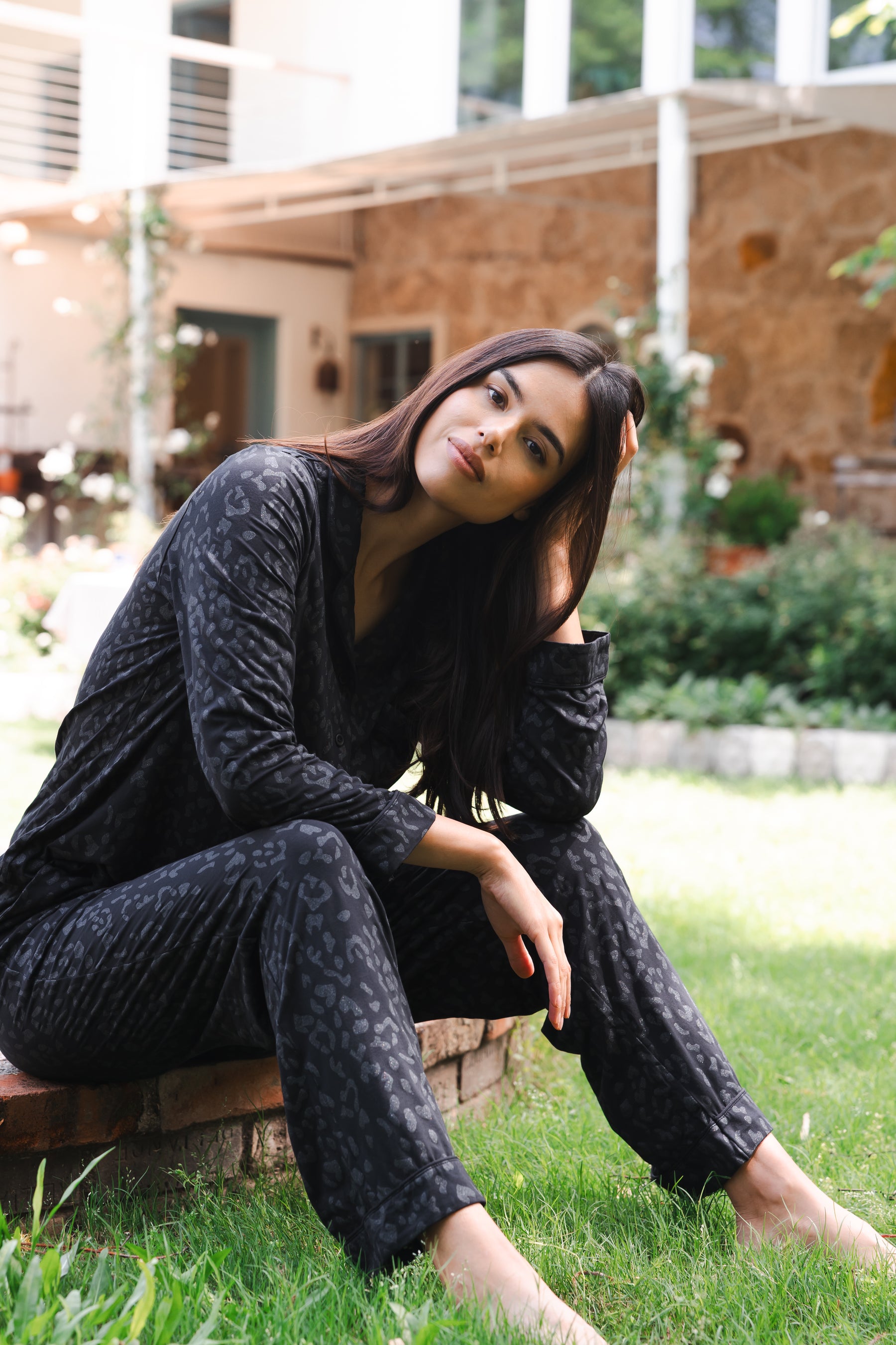 Female sitting outside on a brick step wearing the Long-Sleeved Women's Pajama Set in Midnight Leopard