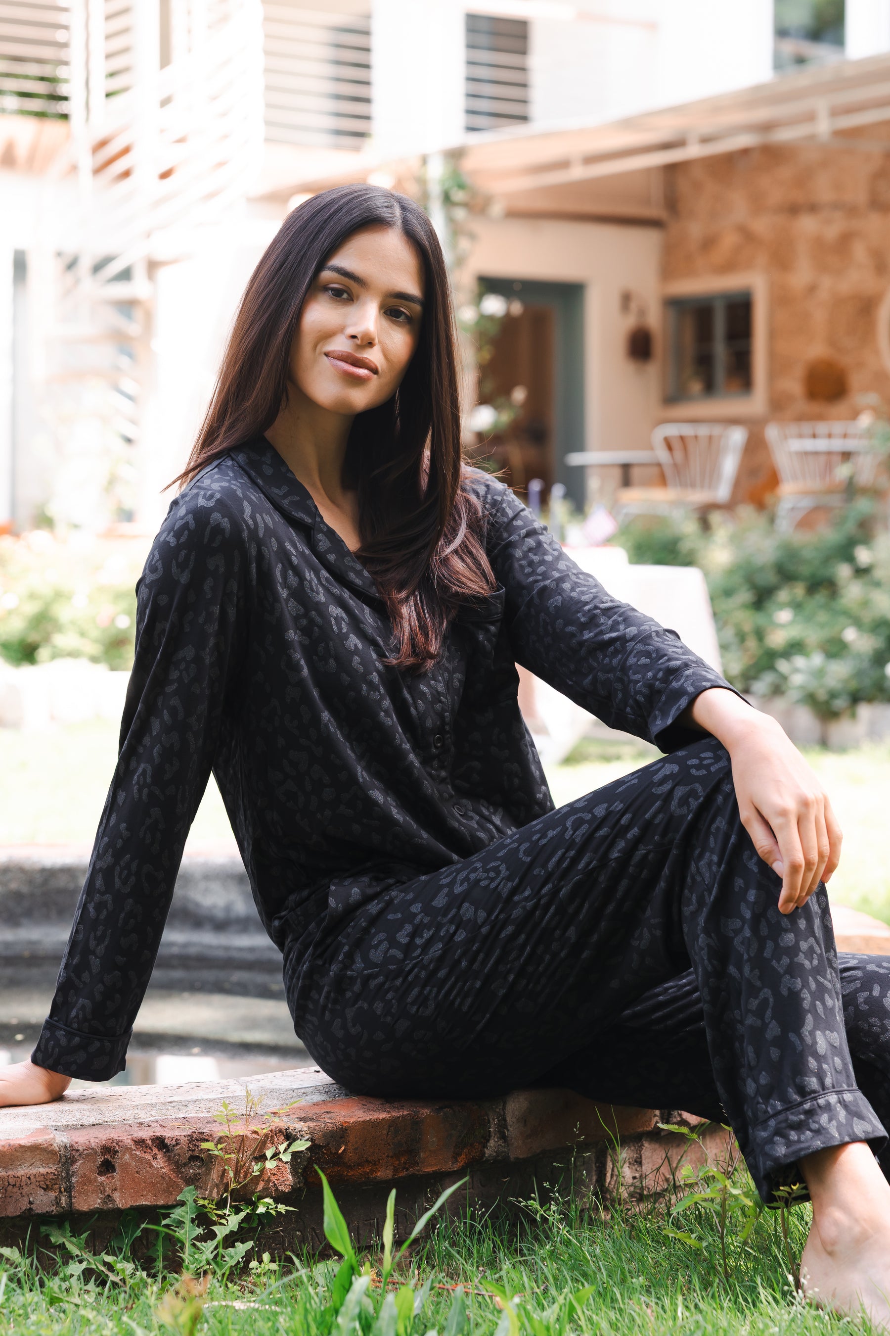 Female sitting on a stone step leaning back wearing the Long-Sleeved Women's Pajama Set in Midnight Leopard