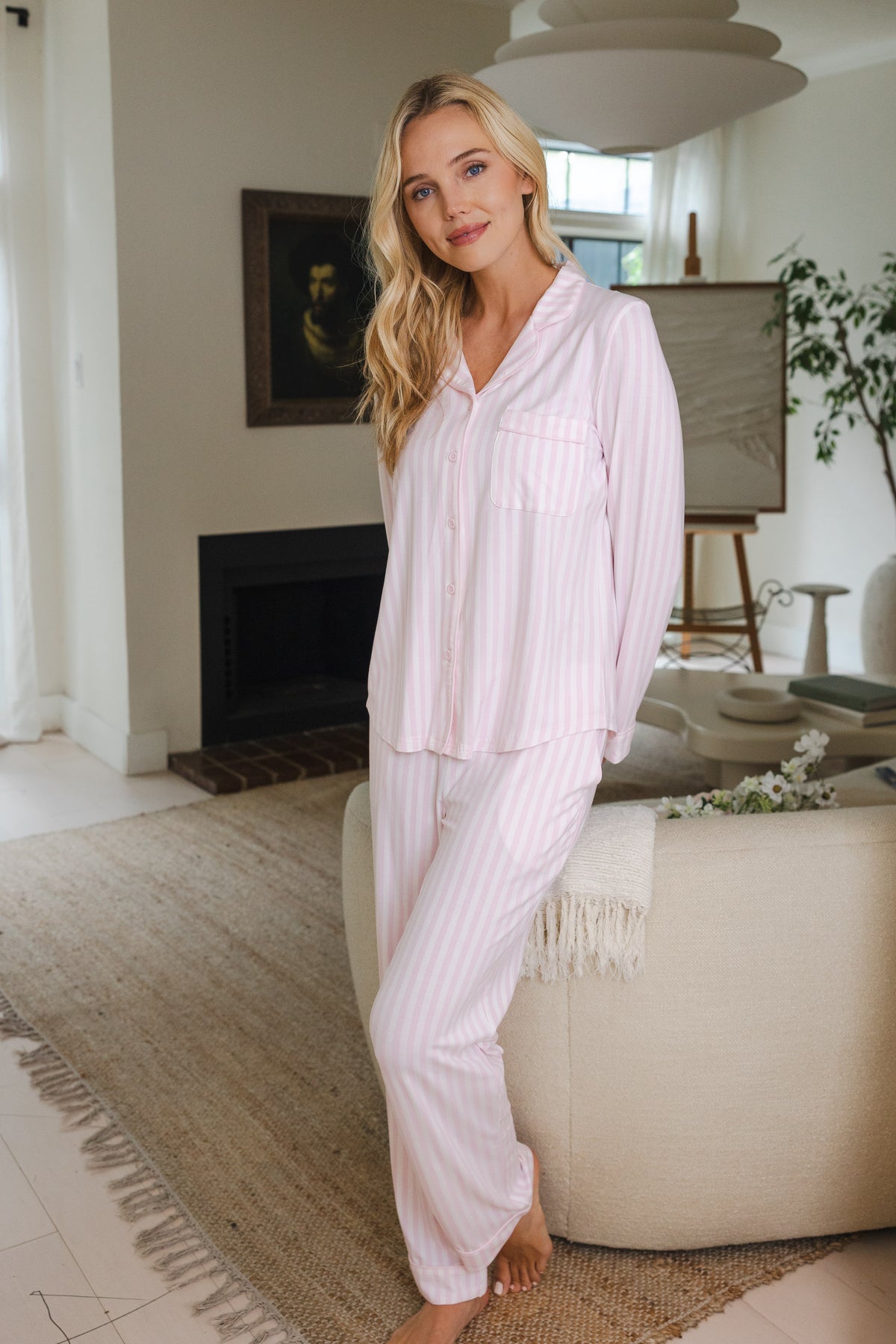Smiling model posing in a living room wearing white and pink stripe pajama set
