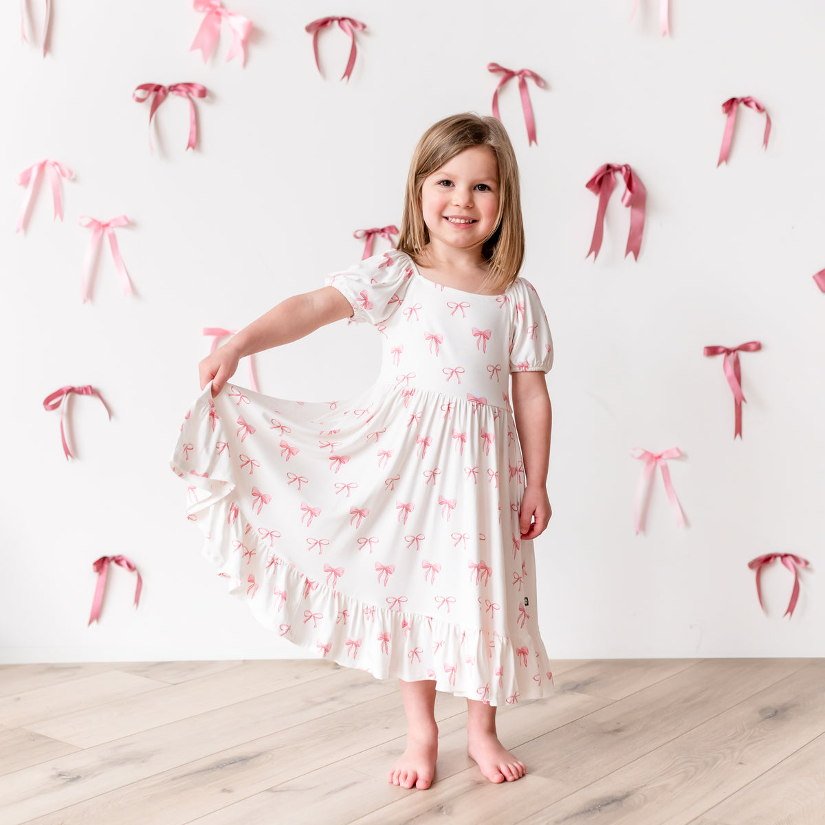 Child modeling Puff Sleeve Twirl Dress in Bow pulling bottom of dress out to show the movement of skirt 