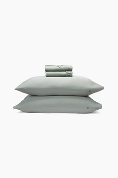 Set of light green bedding including a folded sheet, two pillows, and a sheet on a white background.