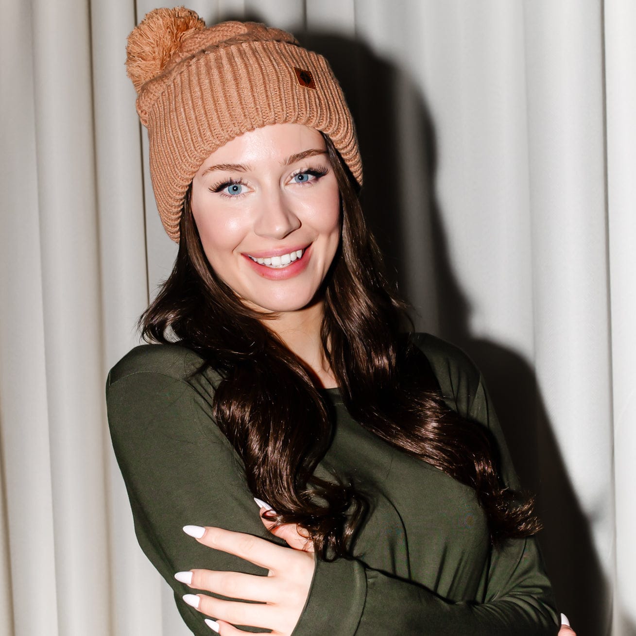 Smiling female modeling the Cable Knit Adult Pom Beanie in Latte