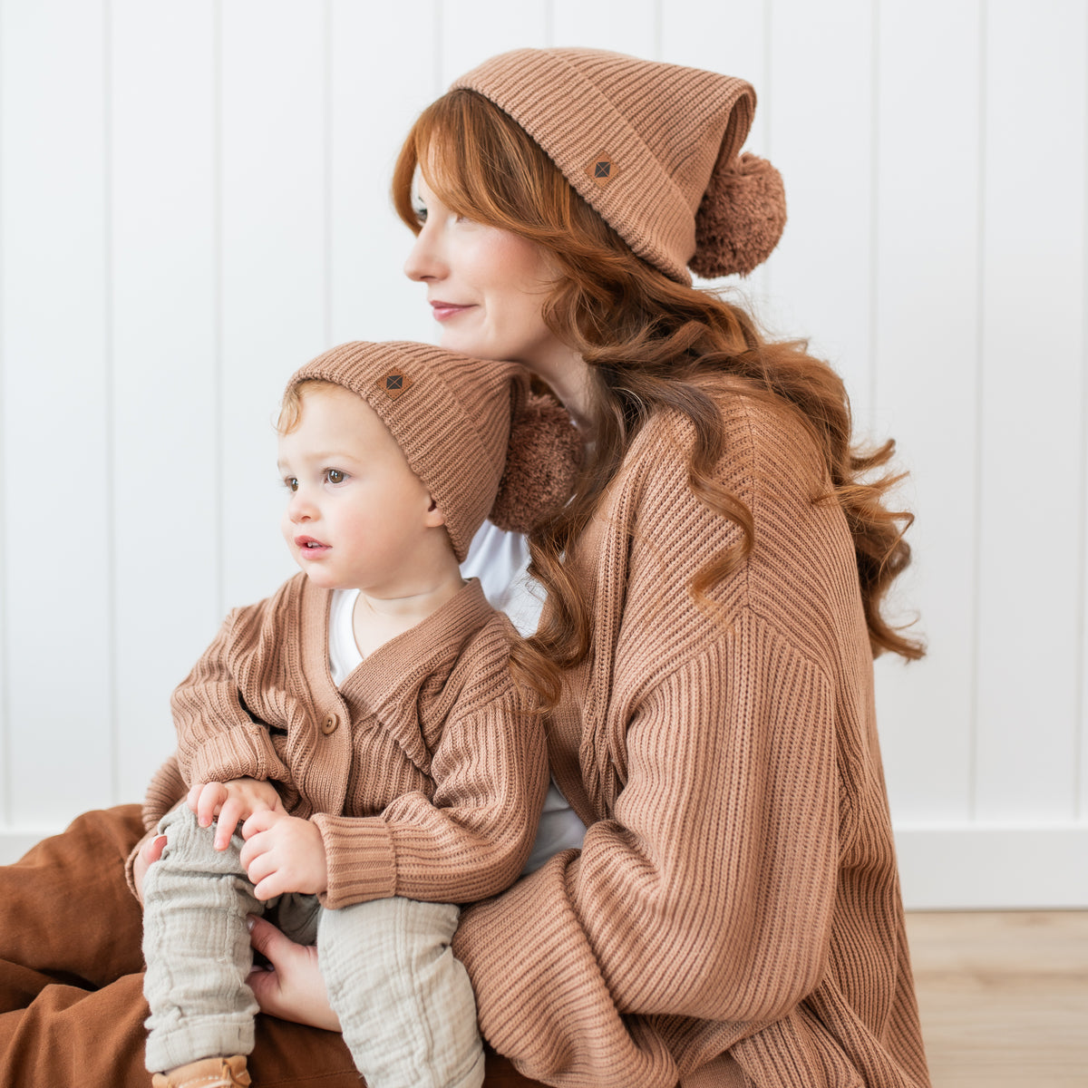 Toddler wearing the Chunky Knit Oversized Cardigan in Latte and matching chunky knit pom beanie hat sitting on his moms lap who is matching in an oversized chunky knit women's cardigan and chunky knit adult pom beanie