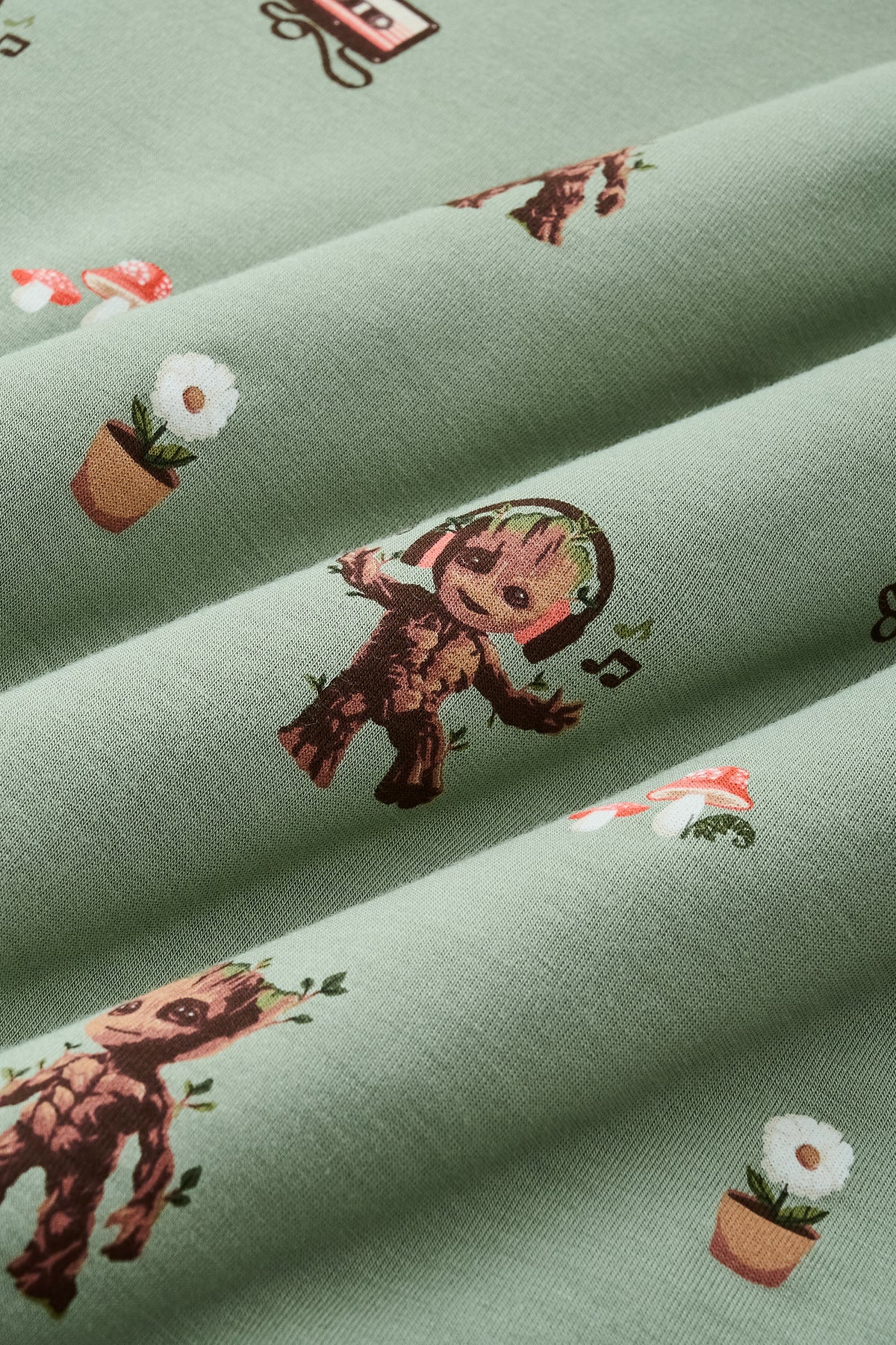 A repeating, all-over print featuring: a standing Baby Groot; a dancing Baby Groot wearing headphones and listening to music; a potted white daisy flower; two toadstools with red caps and white spots; a cluster of ivy; and a cassette tape with tape pulled out, over a dusty sage green background color named Thyme.