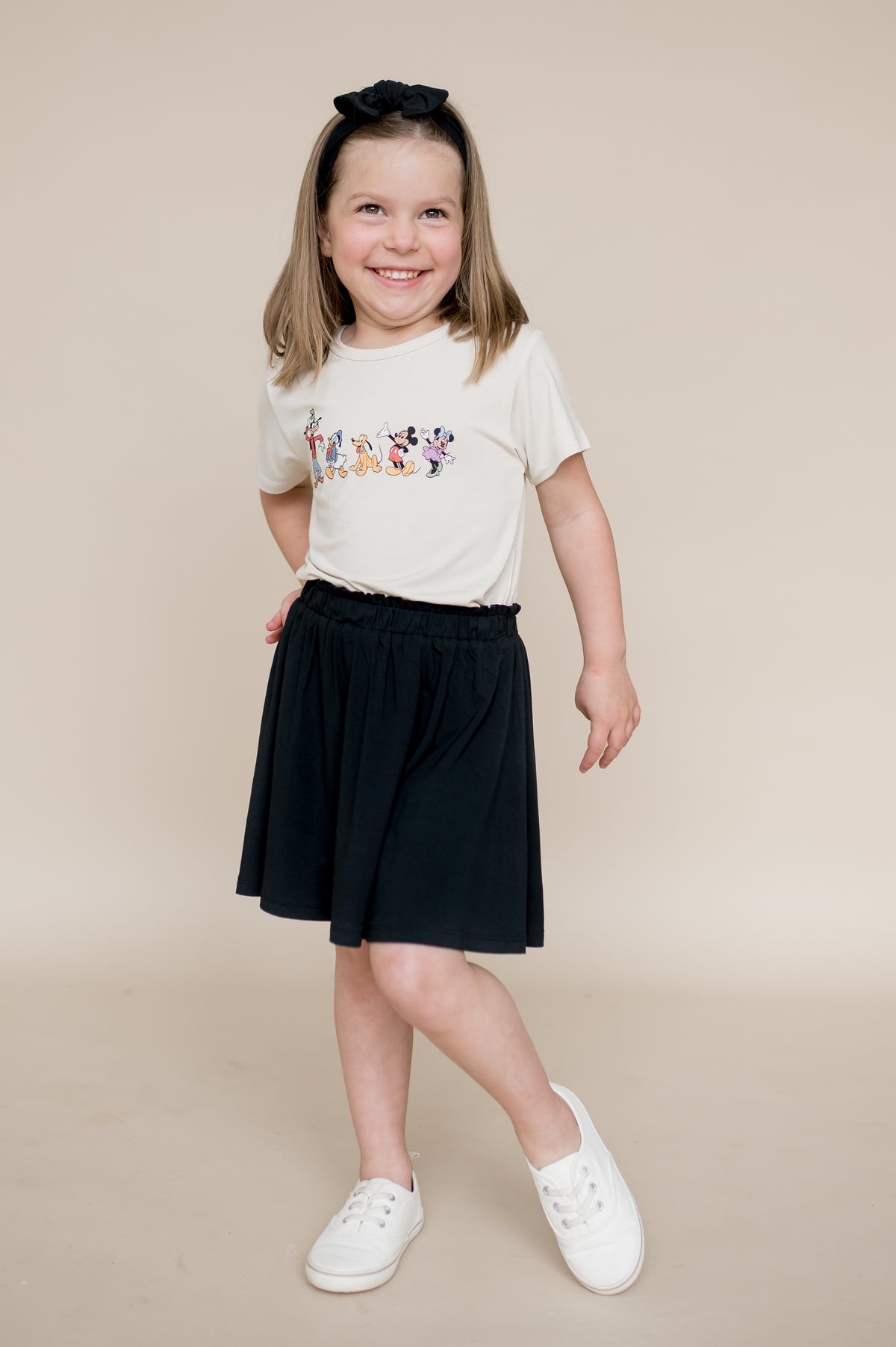 Girl wearing a mickey and friends graphic tee, black bow and black skort