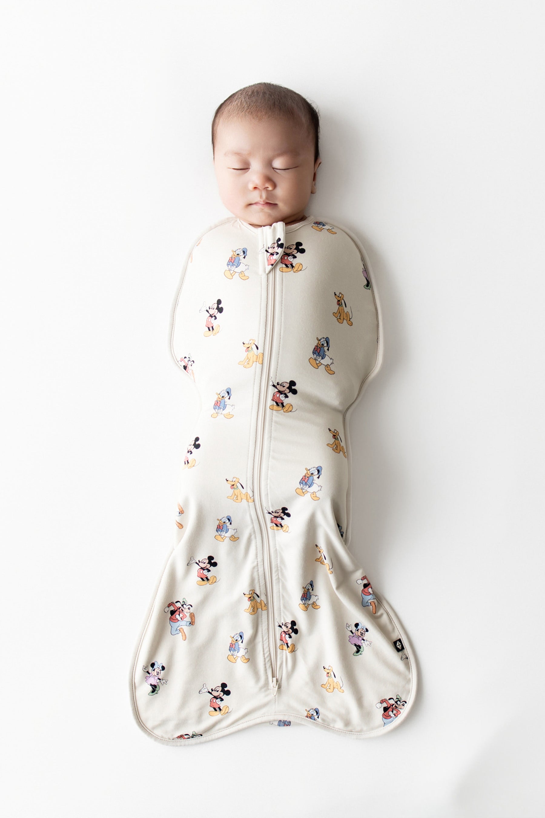 Baby asleep in kyte baby's fuss free swaddle bag with mickey and friends character pattern