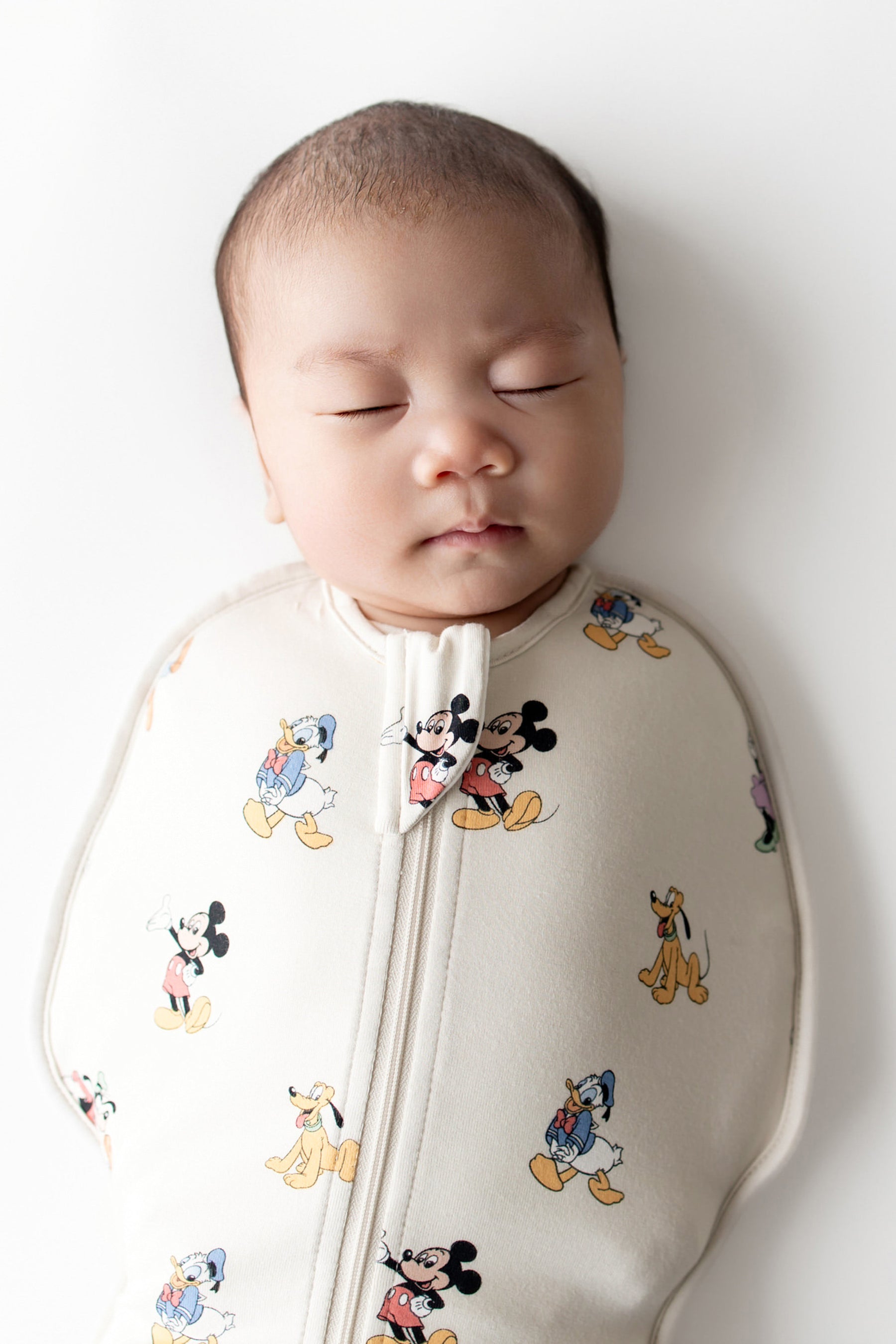 Baby asleep in Mickey and friends patterned swaddle bag