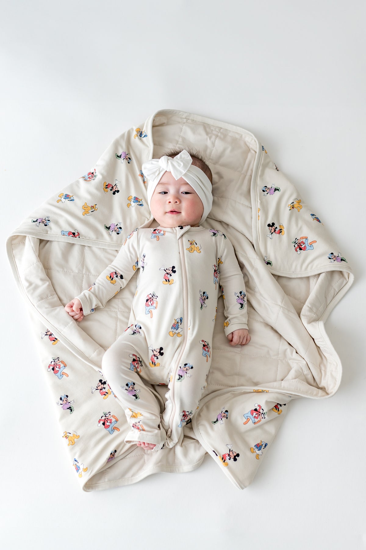 Baby wearing a Mickey Mouse footie laying on a matching baby blanket