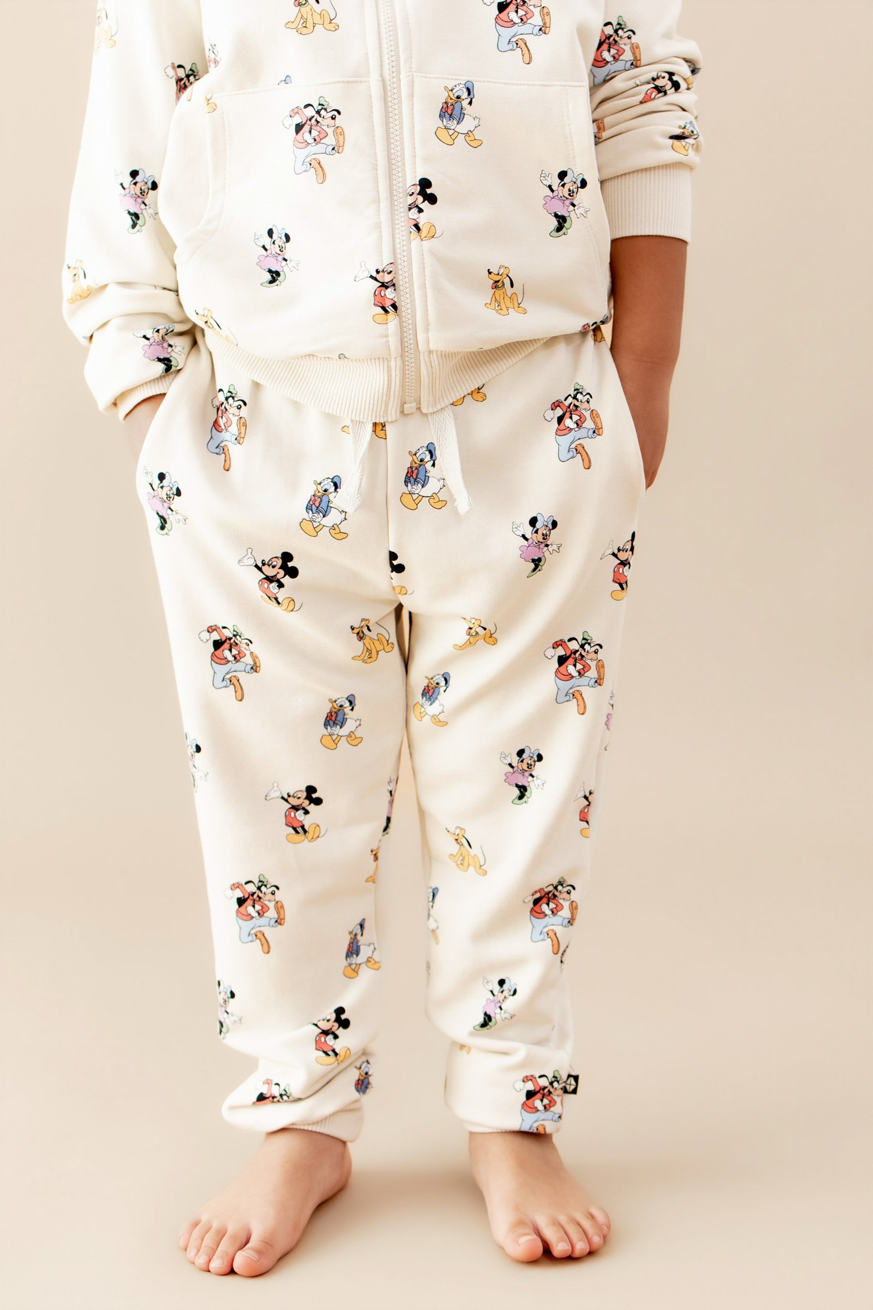 Child wearing a pair of jogger pants with a mickey and friends pattern