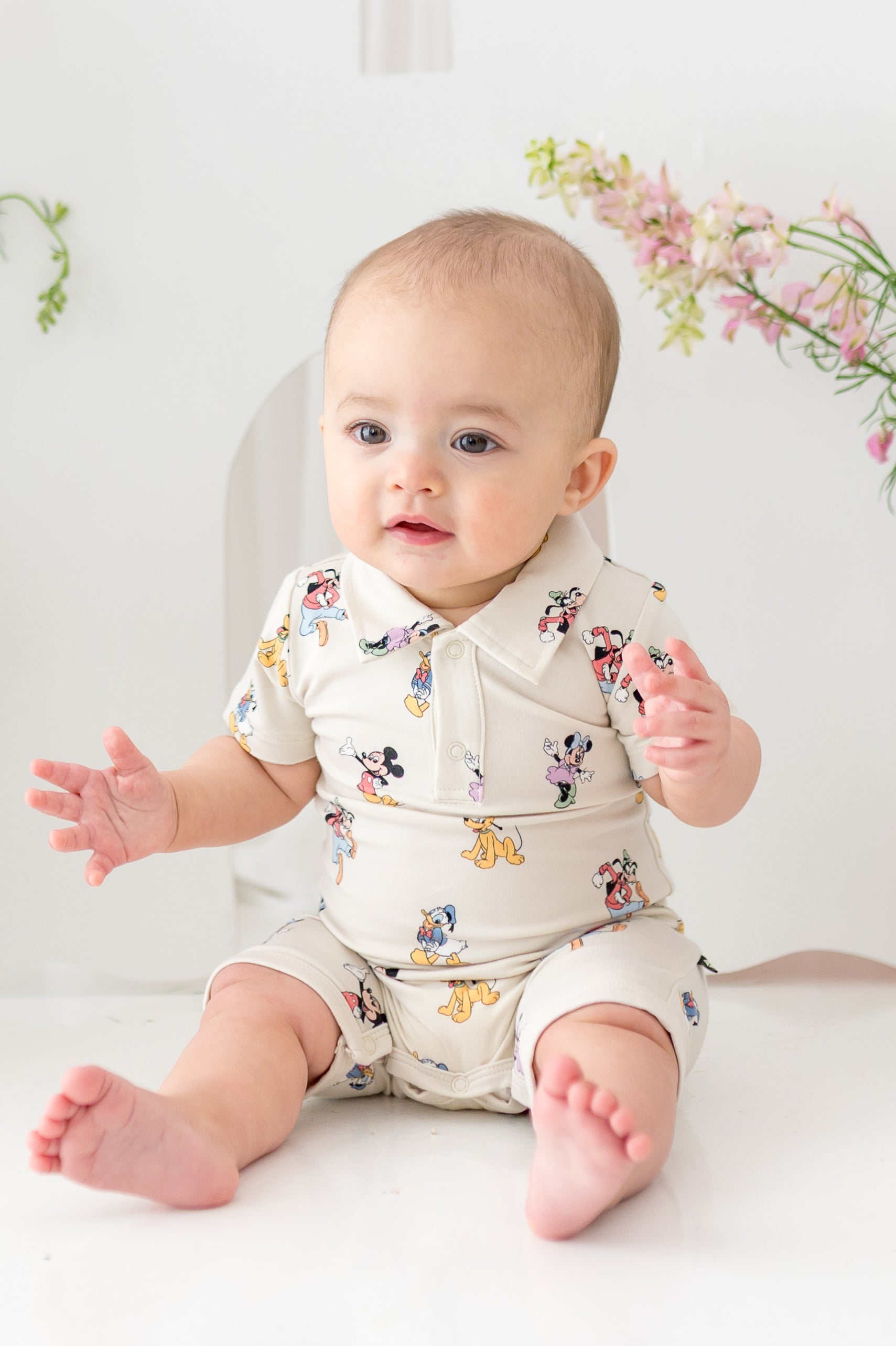 Baby sitting wearing a mickey and friends pattern shortall with polo collar