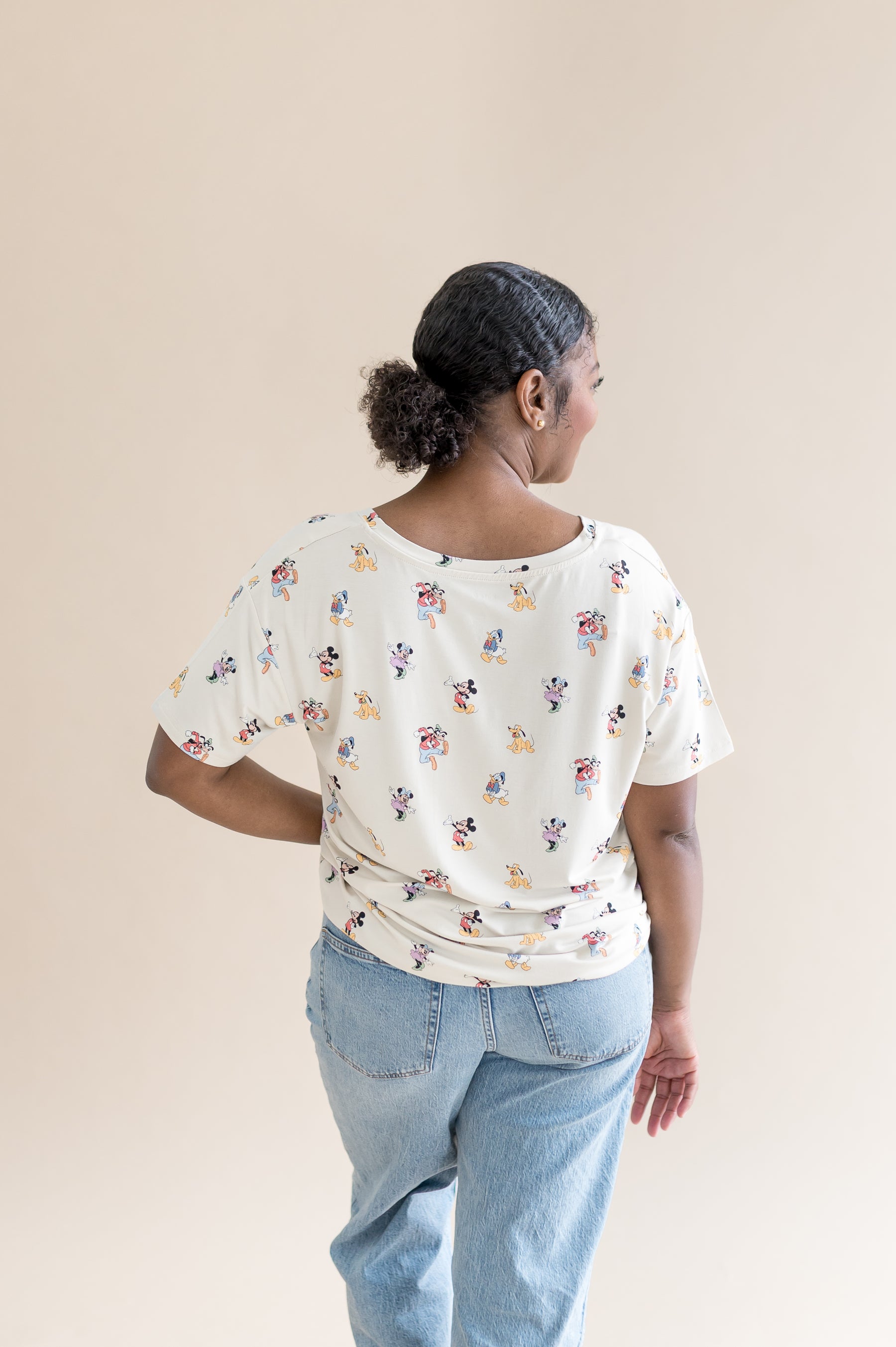 Woman showing the back of the oversized v-neck tshirt that features a pattern of mickey mouse and friends