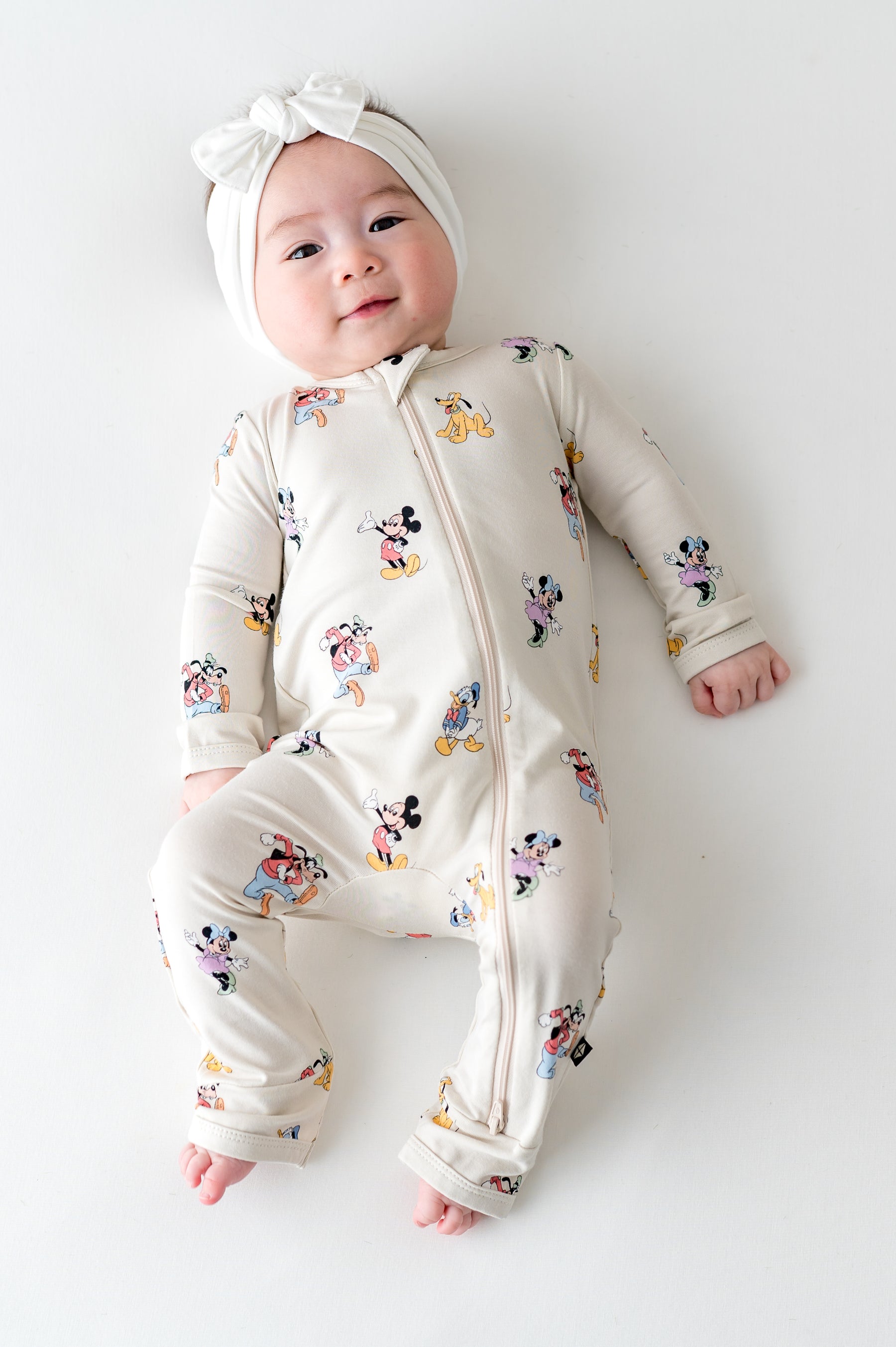 Baby wearing mickey and friends patterned zippered romper and white bow