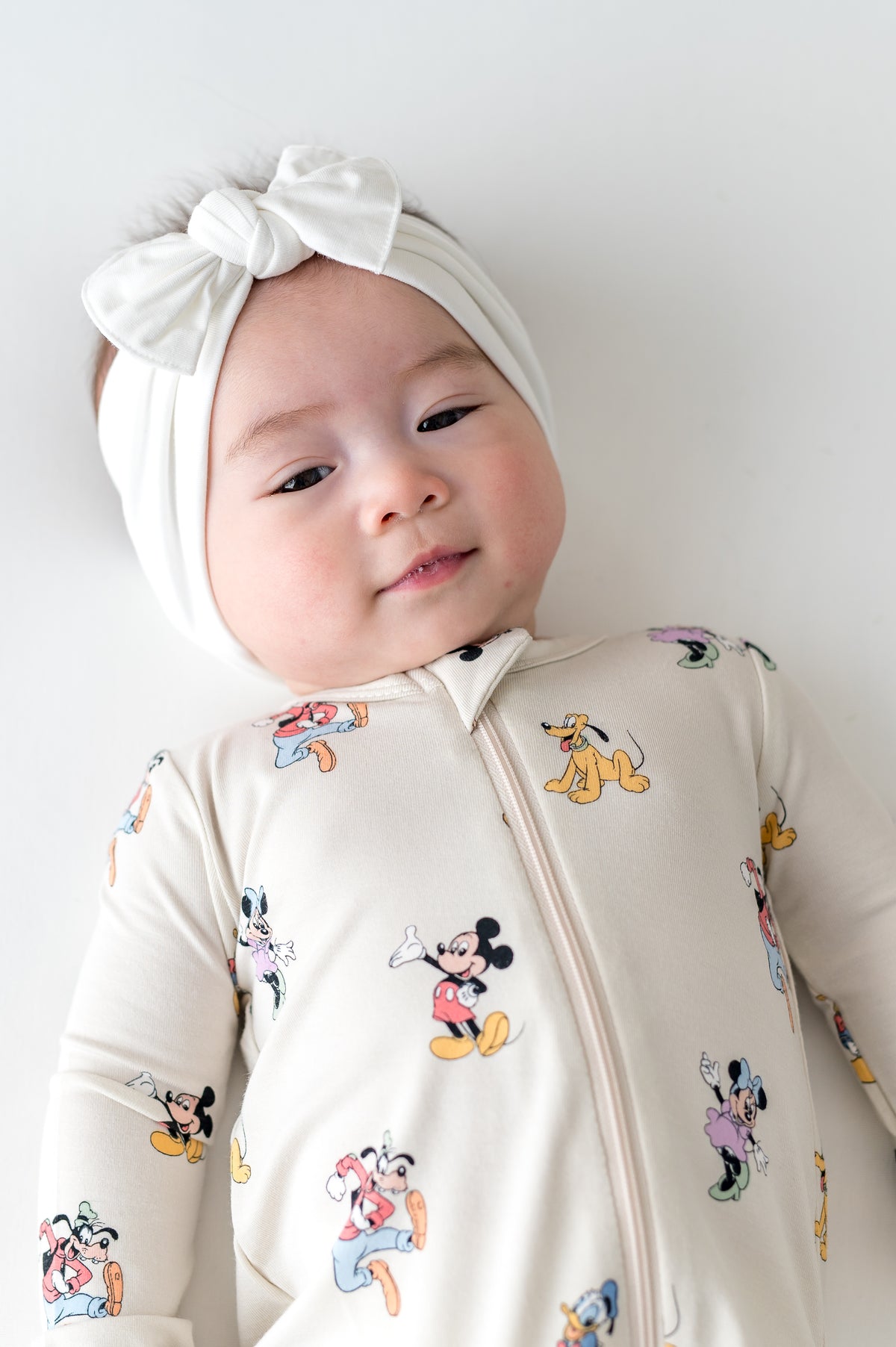 Baby in a zippered onesie with mickey cartoon pattern and white bow