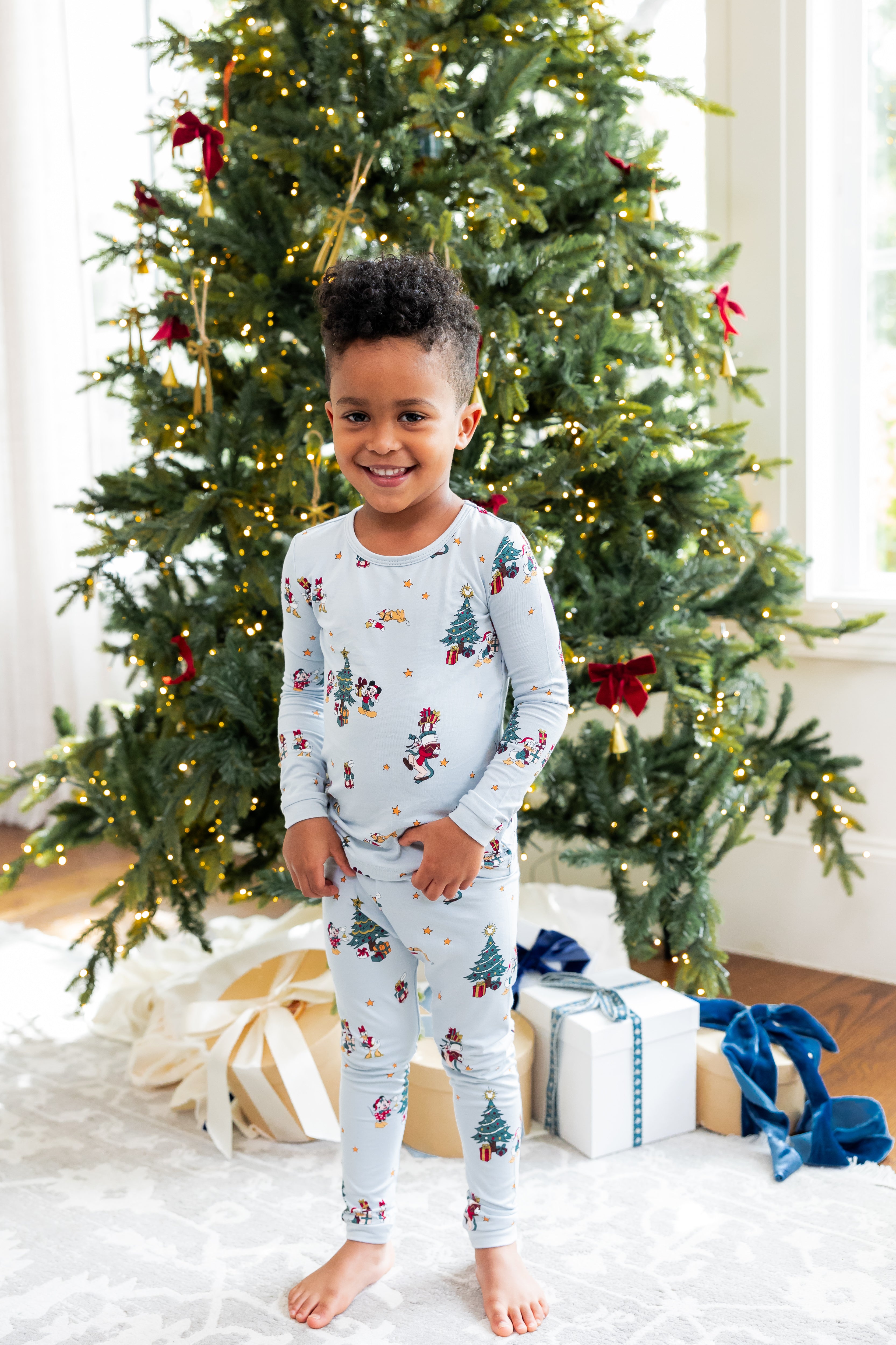 Boy standing in front of Christmas tree and presents wearing Long Sleeve Pajamas in Mickey & Friends Christmas print