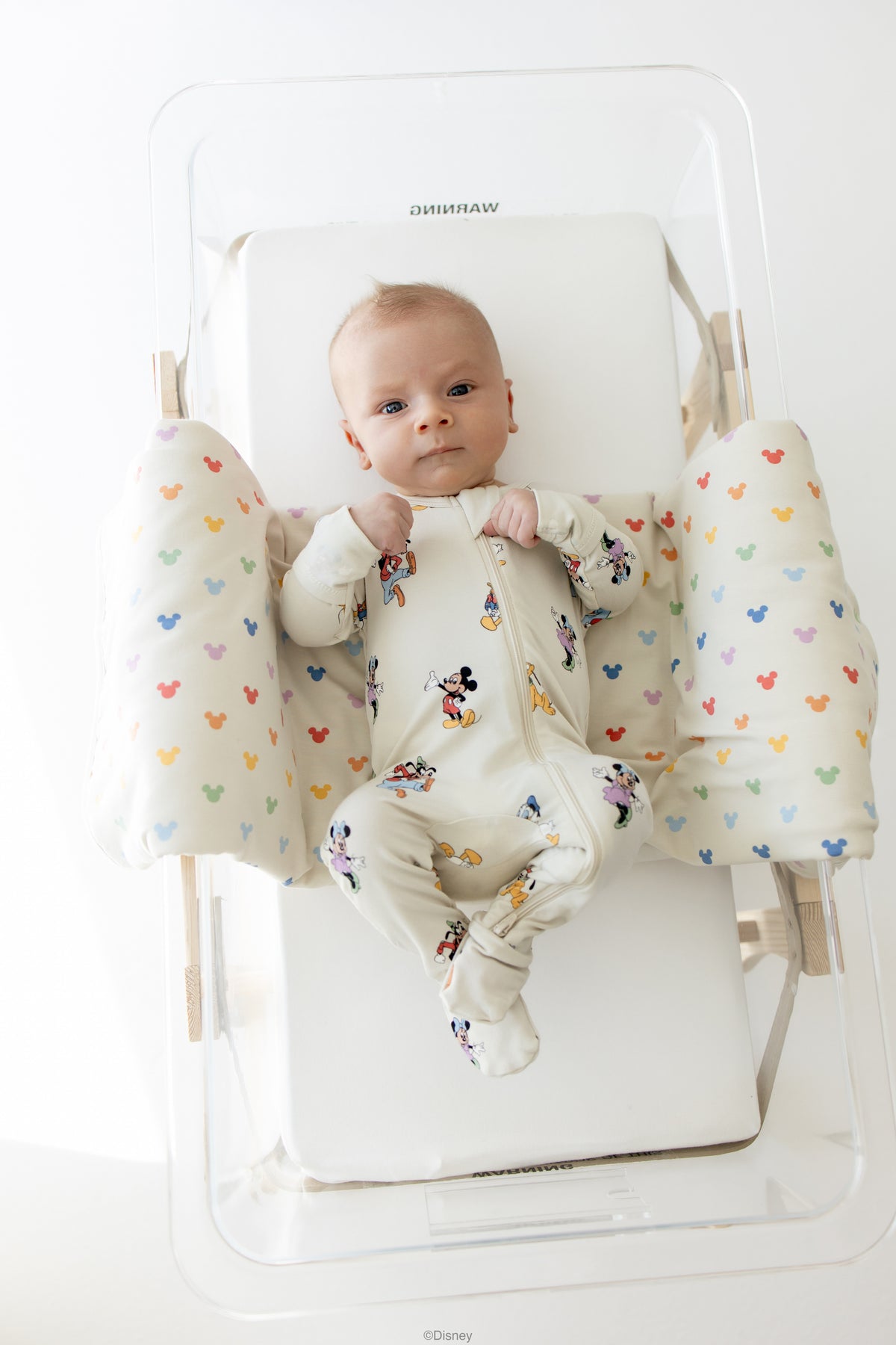 Baby in a mickey mouse and friends footed pajama in a hospital style bassinet 