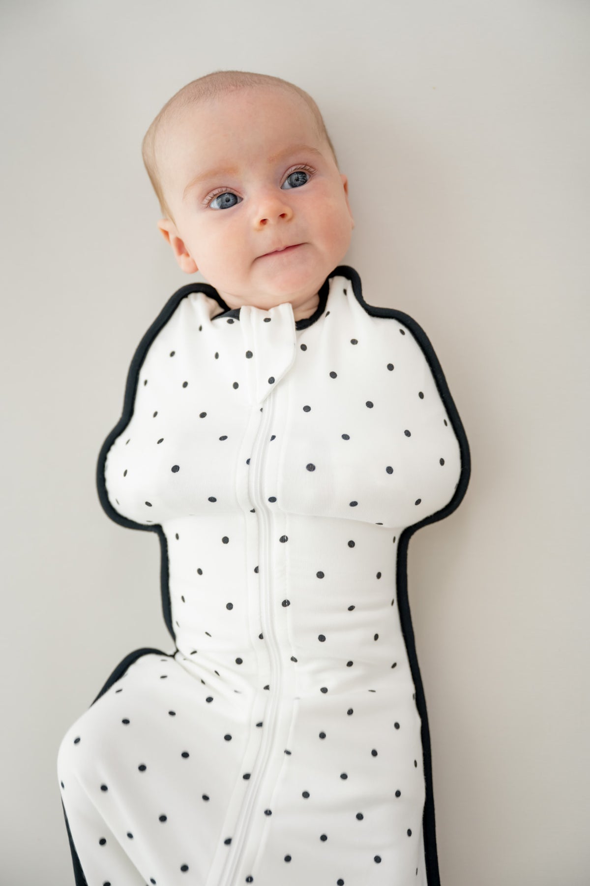 Baby in Swaddle bag with Midnight Polka Dot print on a beige background