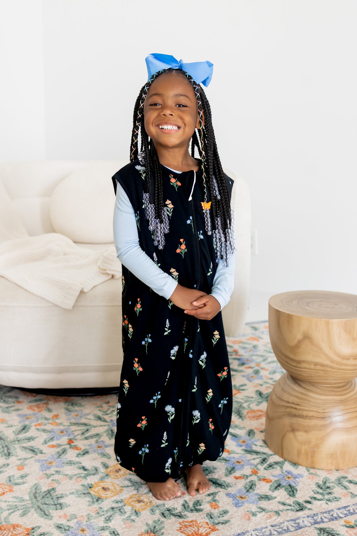 Girl posing in Sleep Bag Walker in Midnight Wildflower 1.0 print with a blue bow on head standing in a living room