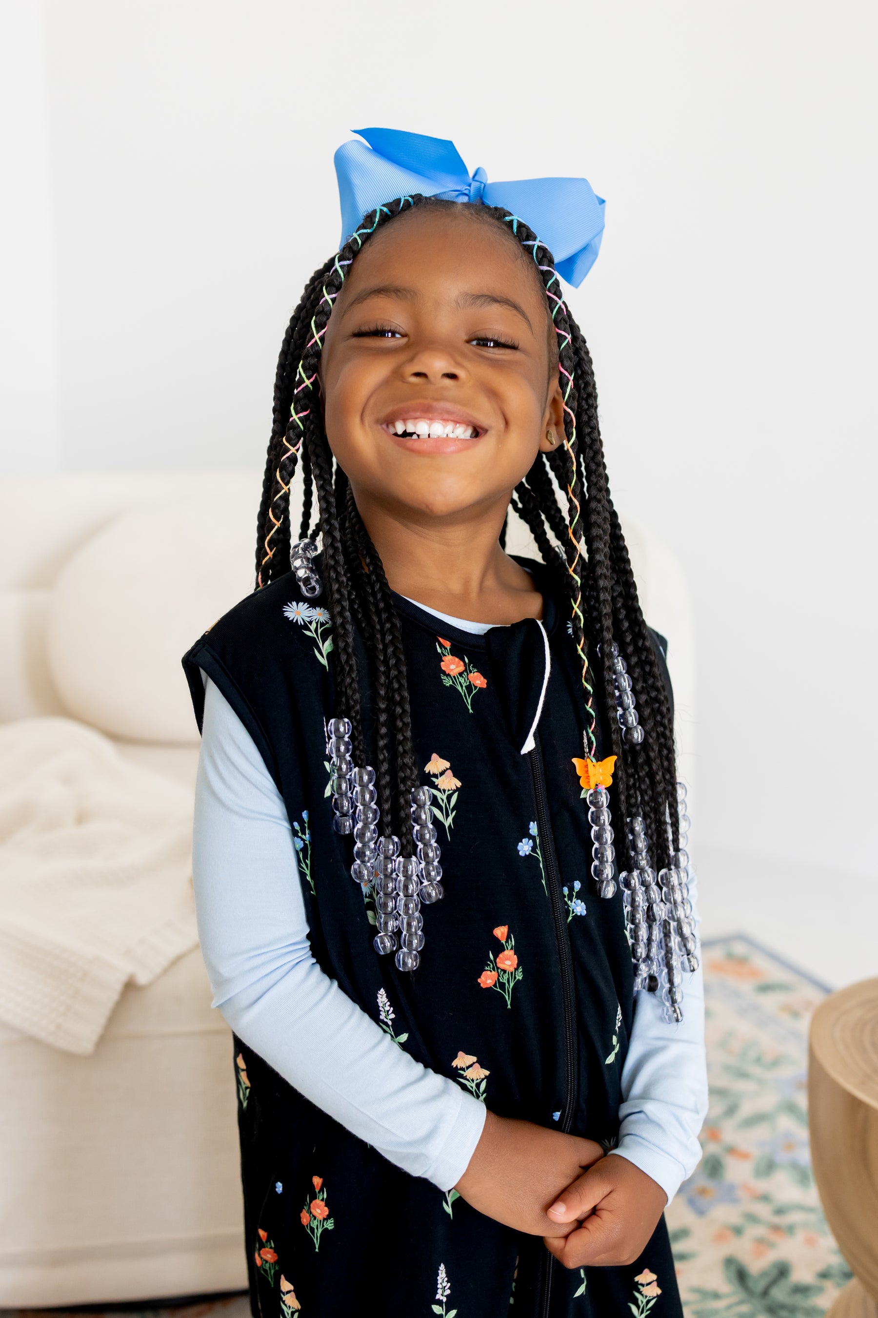 Girl smiling in Sleep Bag Walker in Midnight Wildflower 1.0 print with a blue bow on head in front of a white sofa